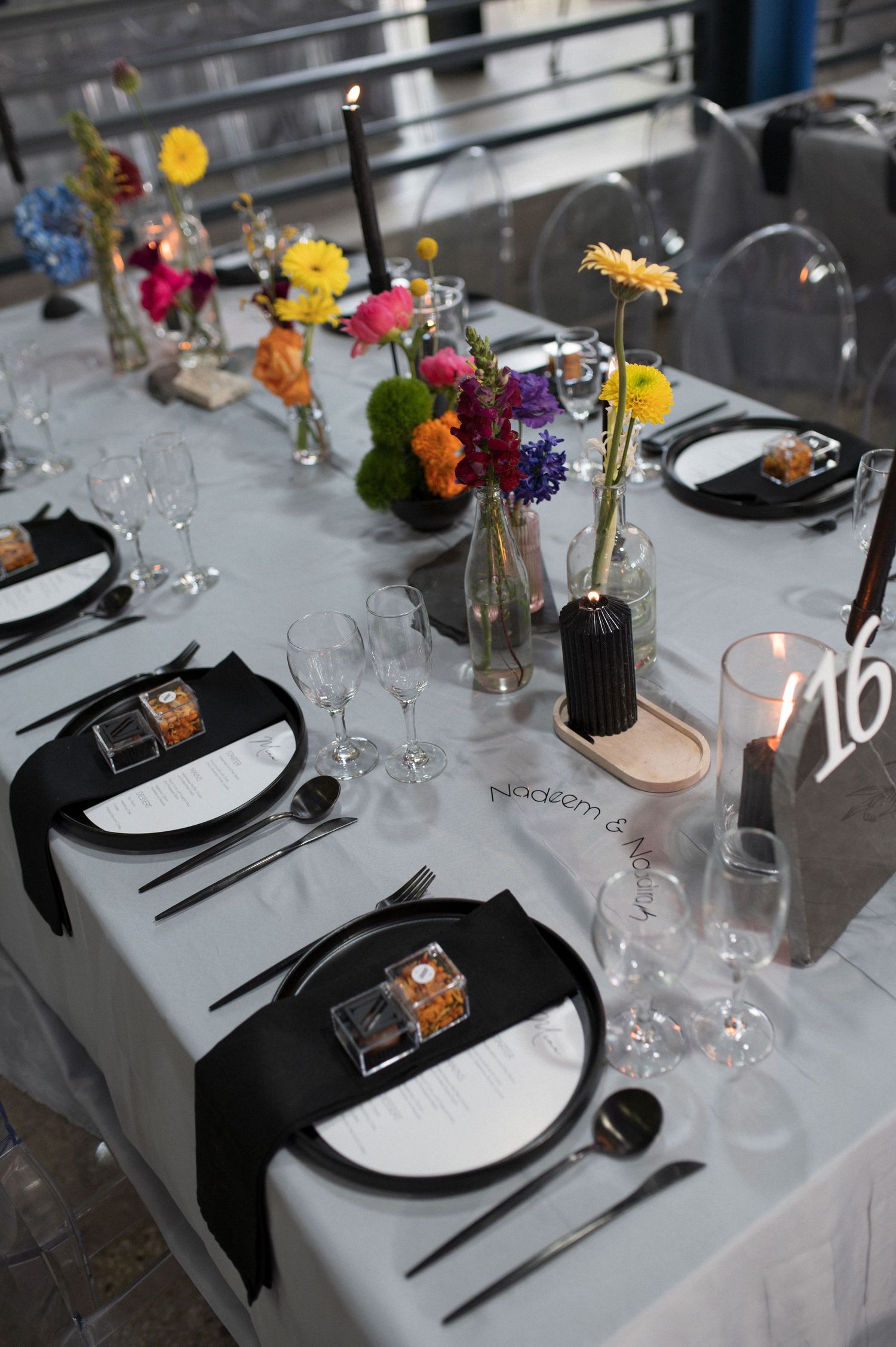 Contemporary table setting with vibrant wildflower centerpieces and black plates on light gray tablecloth.