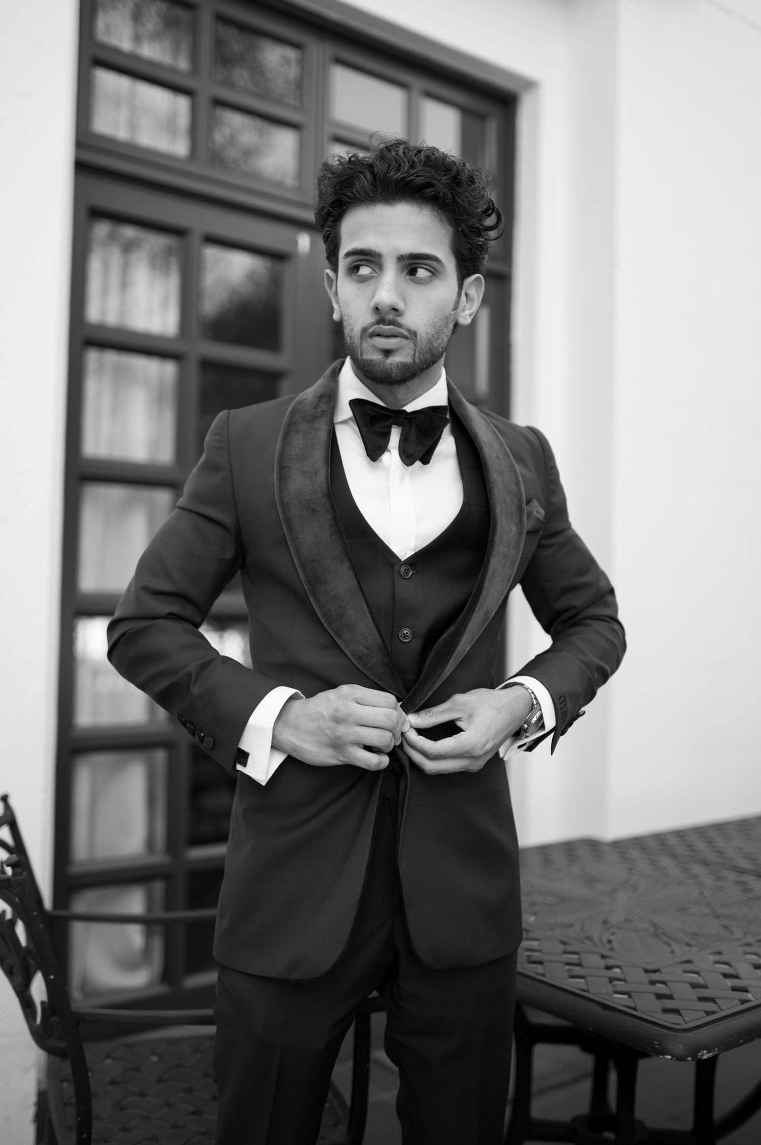 Sophisticated groom in black tuxedo and bow tie against classic building facade.