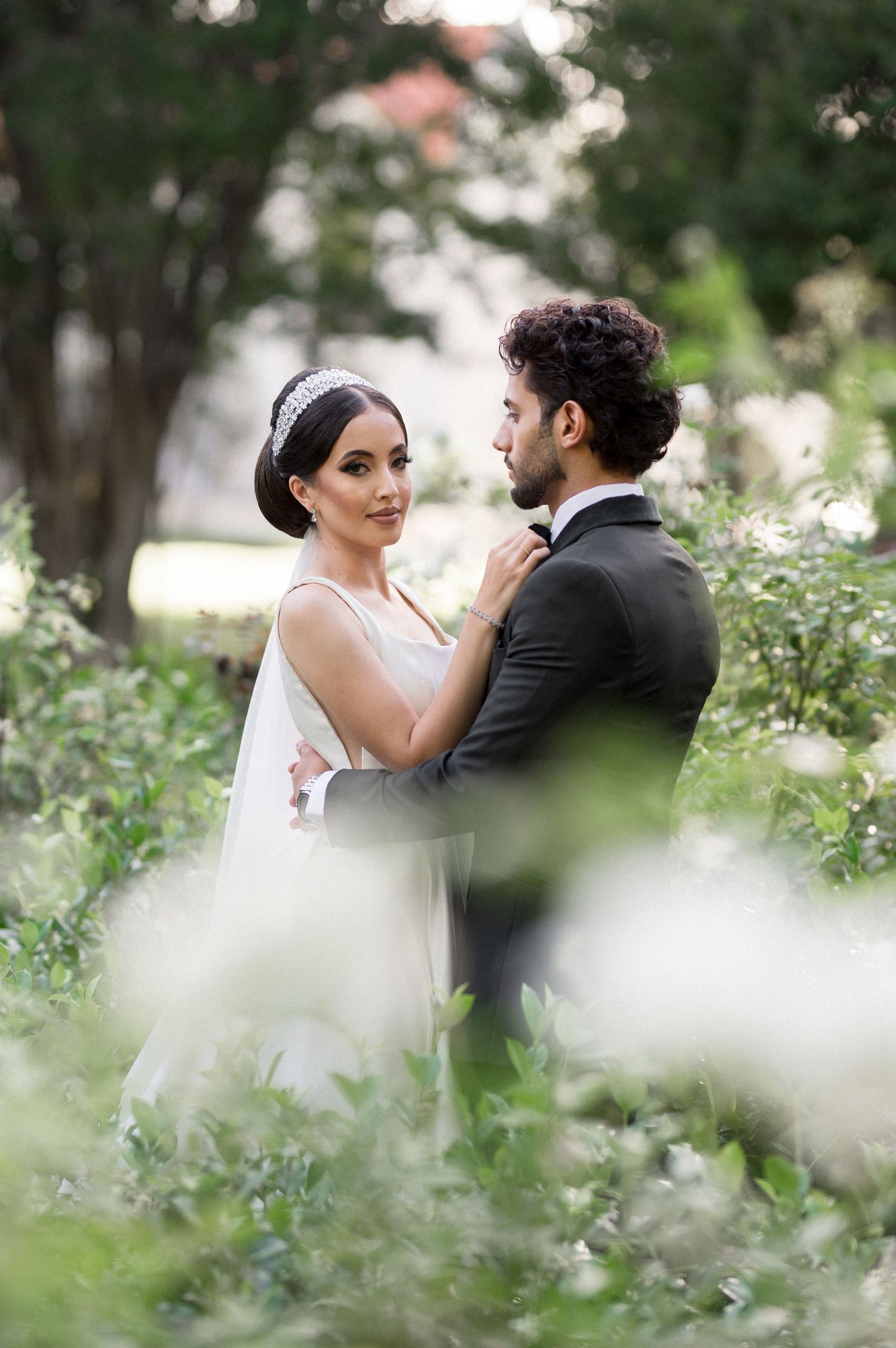 A romantic garden wedding photo with couple embracing among white flowers and greenery.