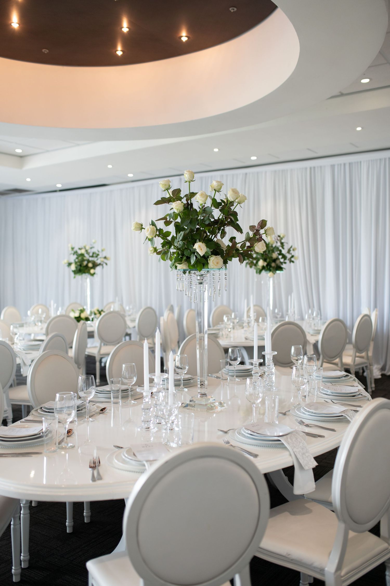 Elegant wedding reception table with white floral centerpiece and modern white chairs.