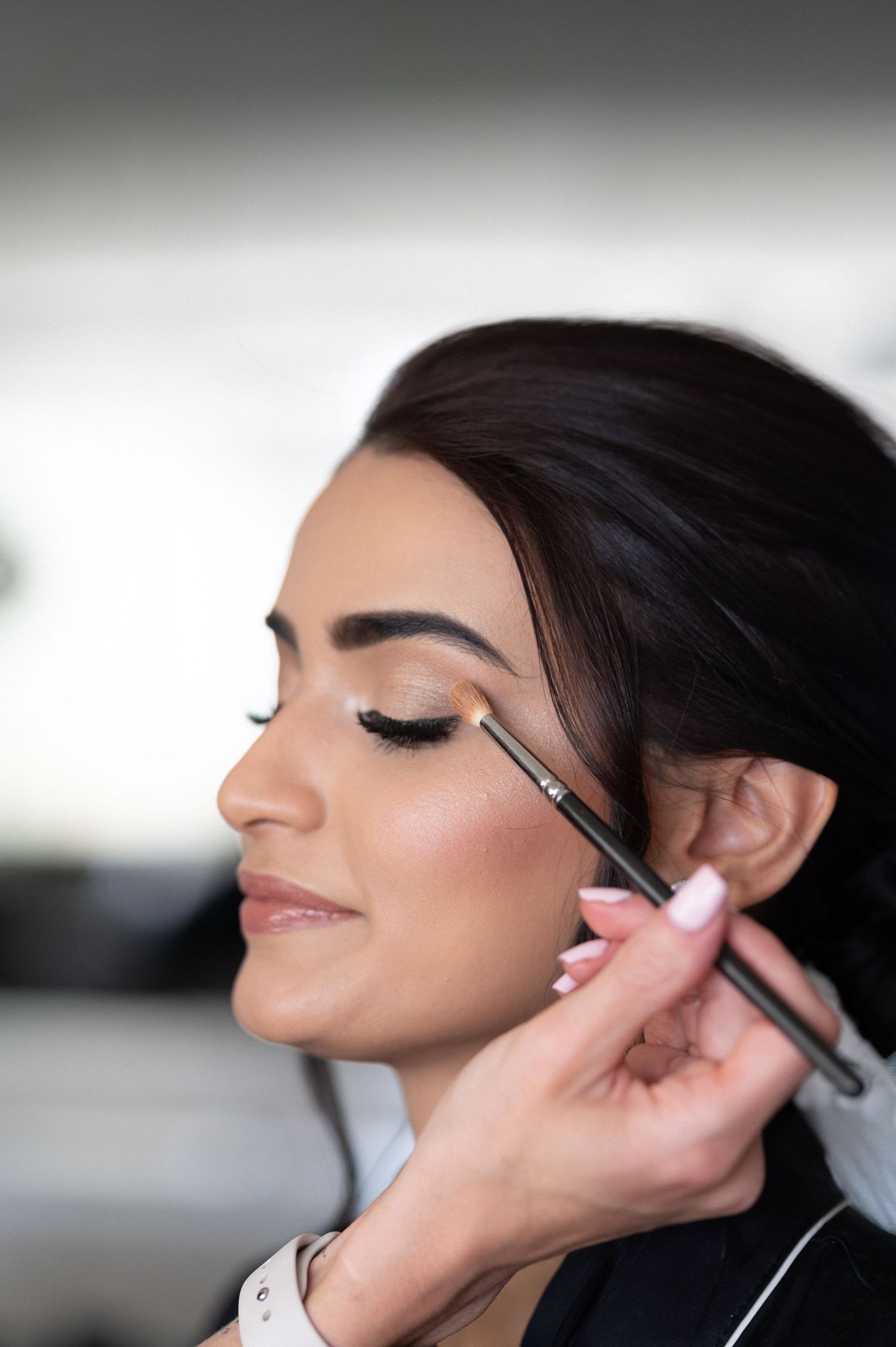 Professional makeup artist applying eyeshadow with a brush during bridal preparation.
