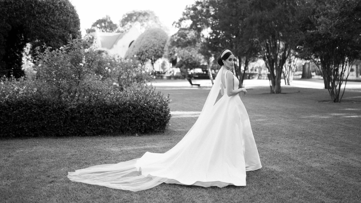 Black and white photo of a wedding gown with long train in an outdoor garden setting.