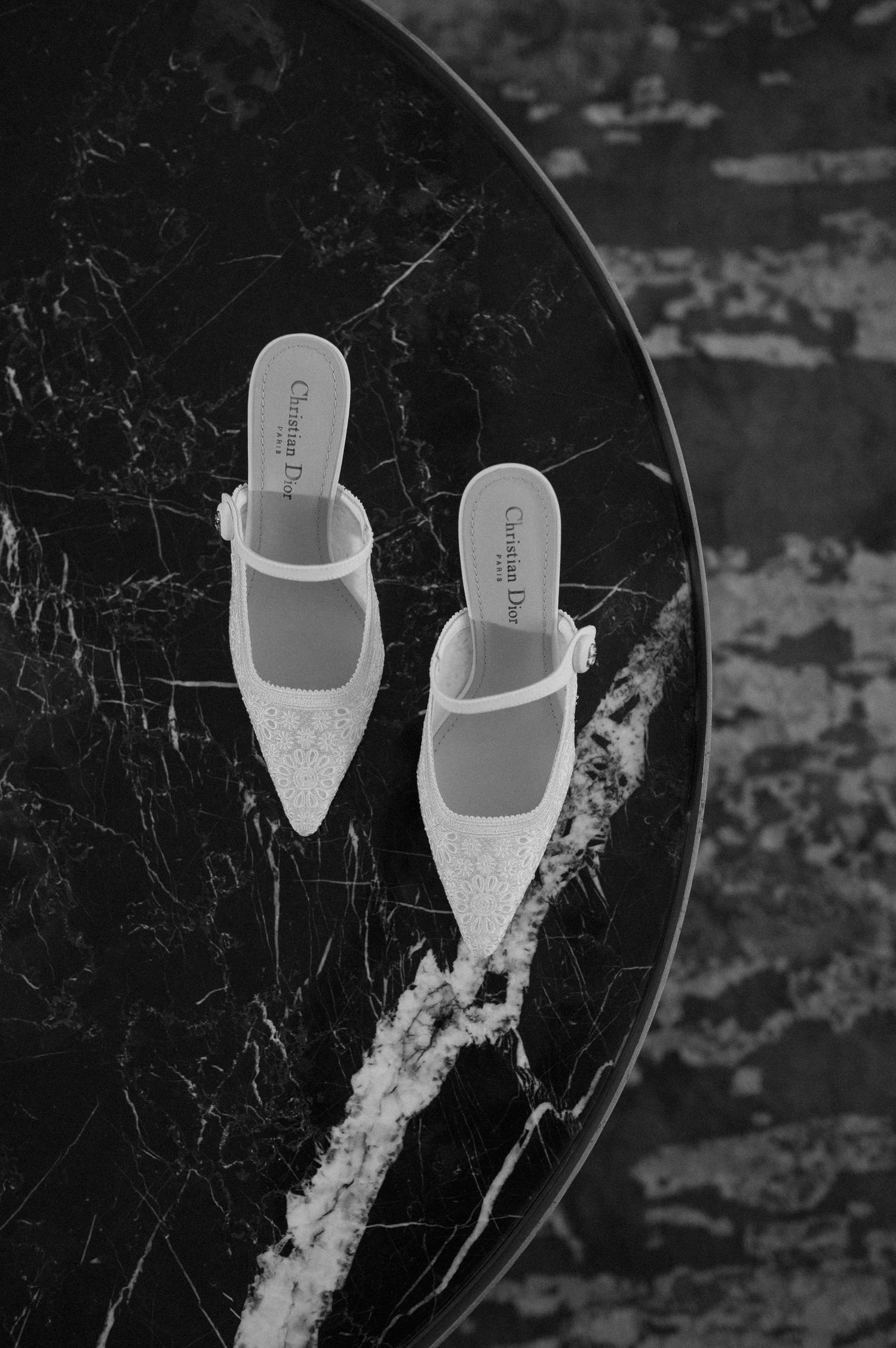 Elegant white bridal shoes displayed on a black marble surface in monochrome.