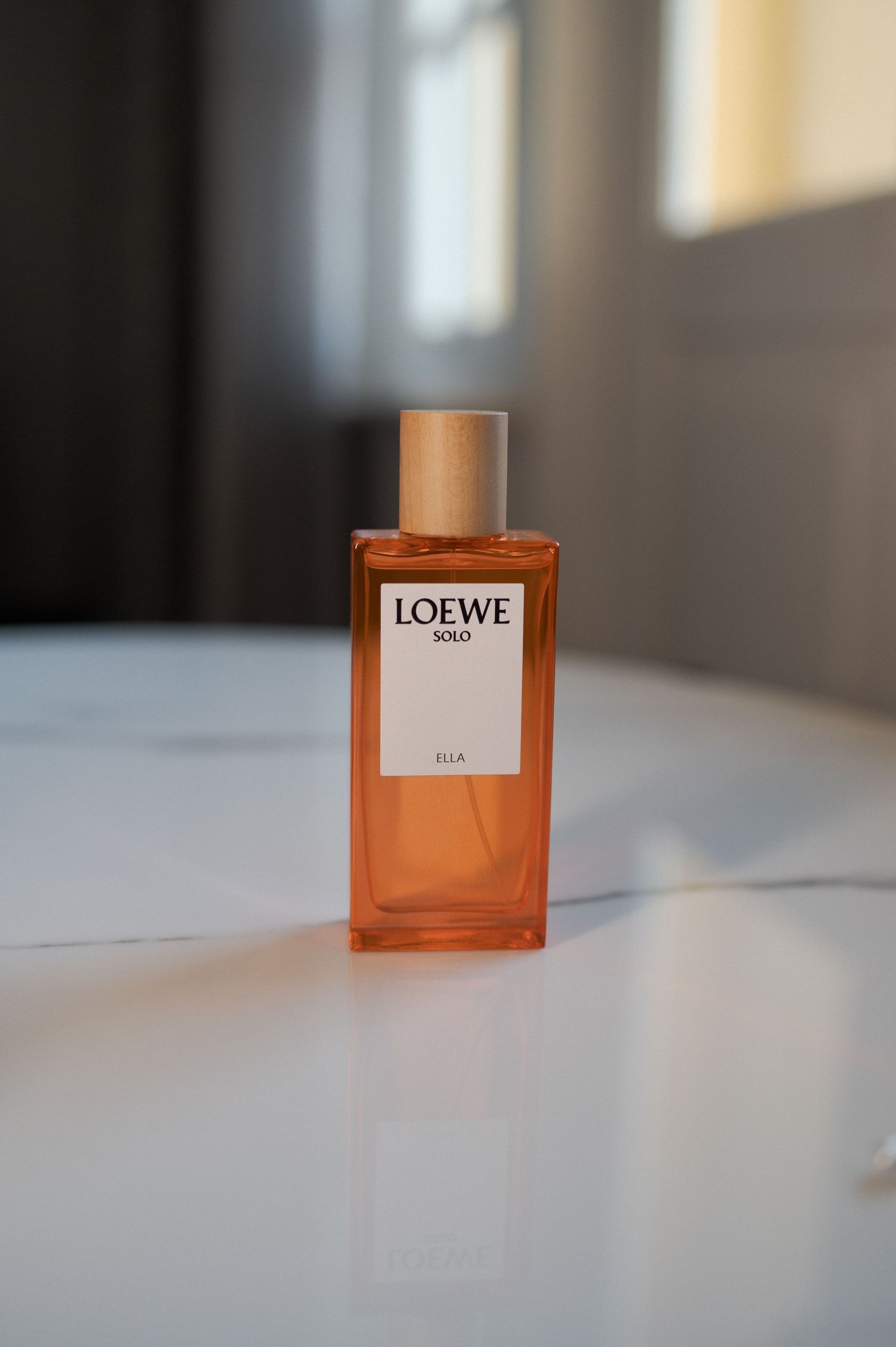 A bottle of Loewe perfume in amber glass sits on a white surface in soft lighting.