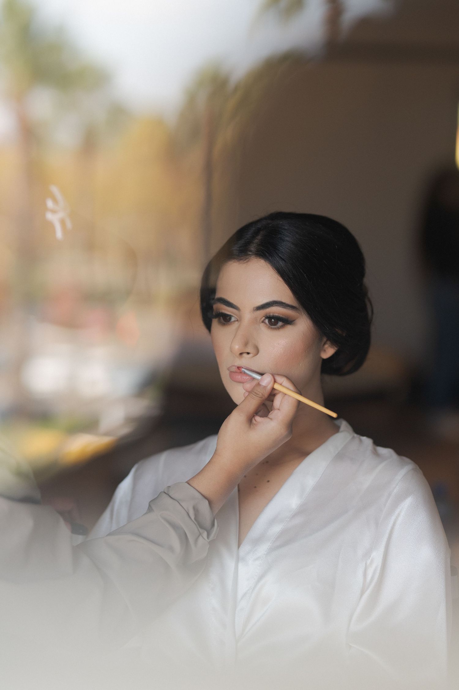 Person getting makeup applied while wearing white robe during wedding preparations.