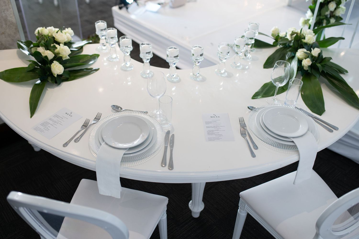 Elegant white table setting with floral arrangements and glassware at a formal event.