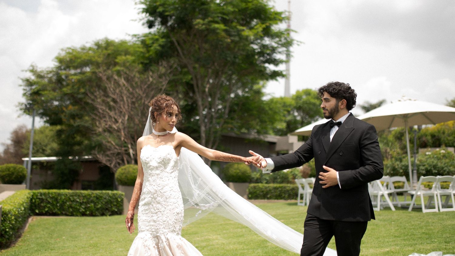 A couple spins playfully on their wedding day with white chairs and garden setting in background.