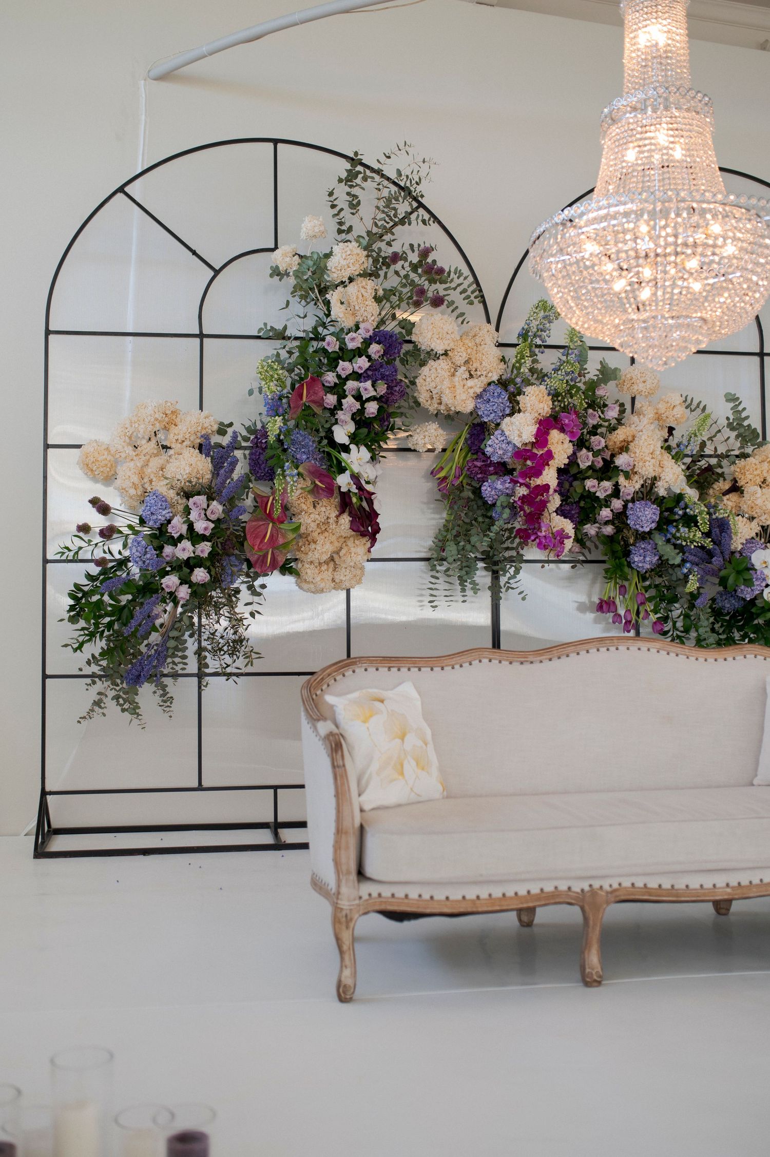 Ornate floral arch display with crystal chandelier and vintage cream sofa.