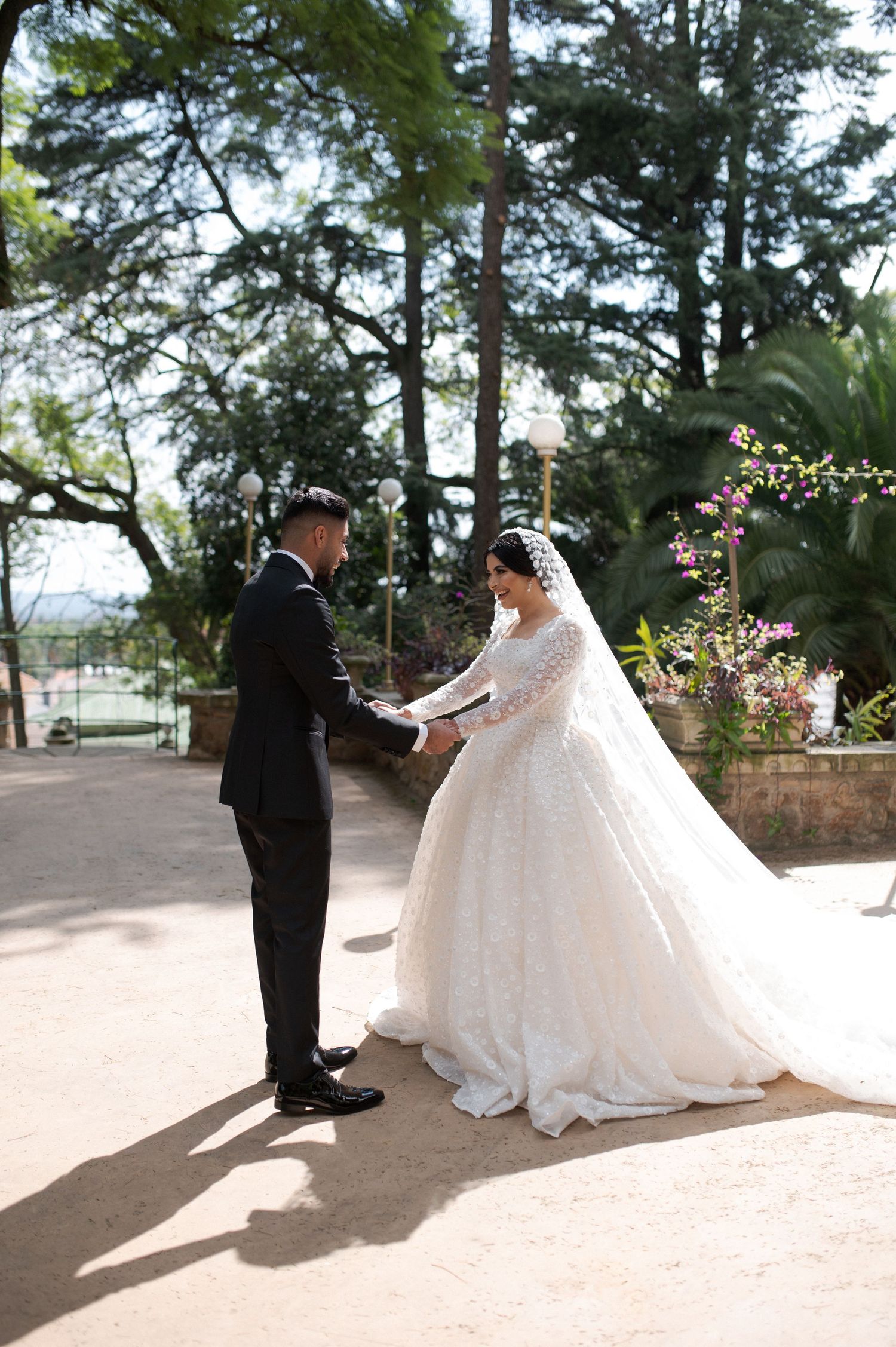 Couple shares intimate moment on garden pathway surrounded by tall pine trees.