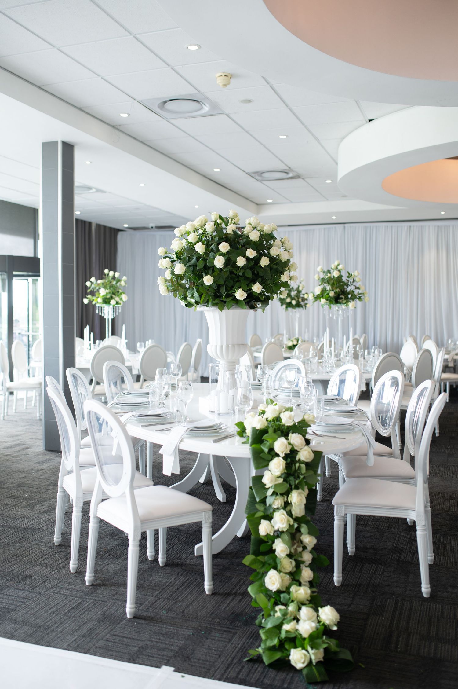Modern wedding reception setup with cascading white rose arrangements and elegant white chairs.
