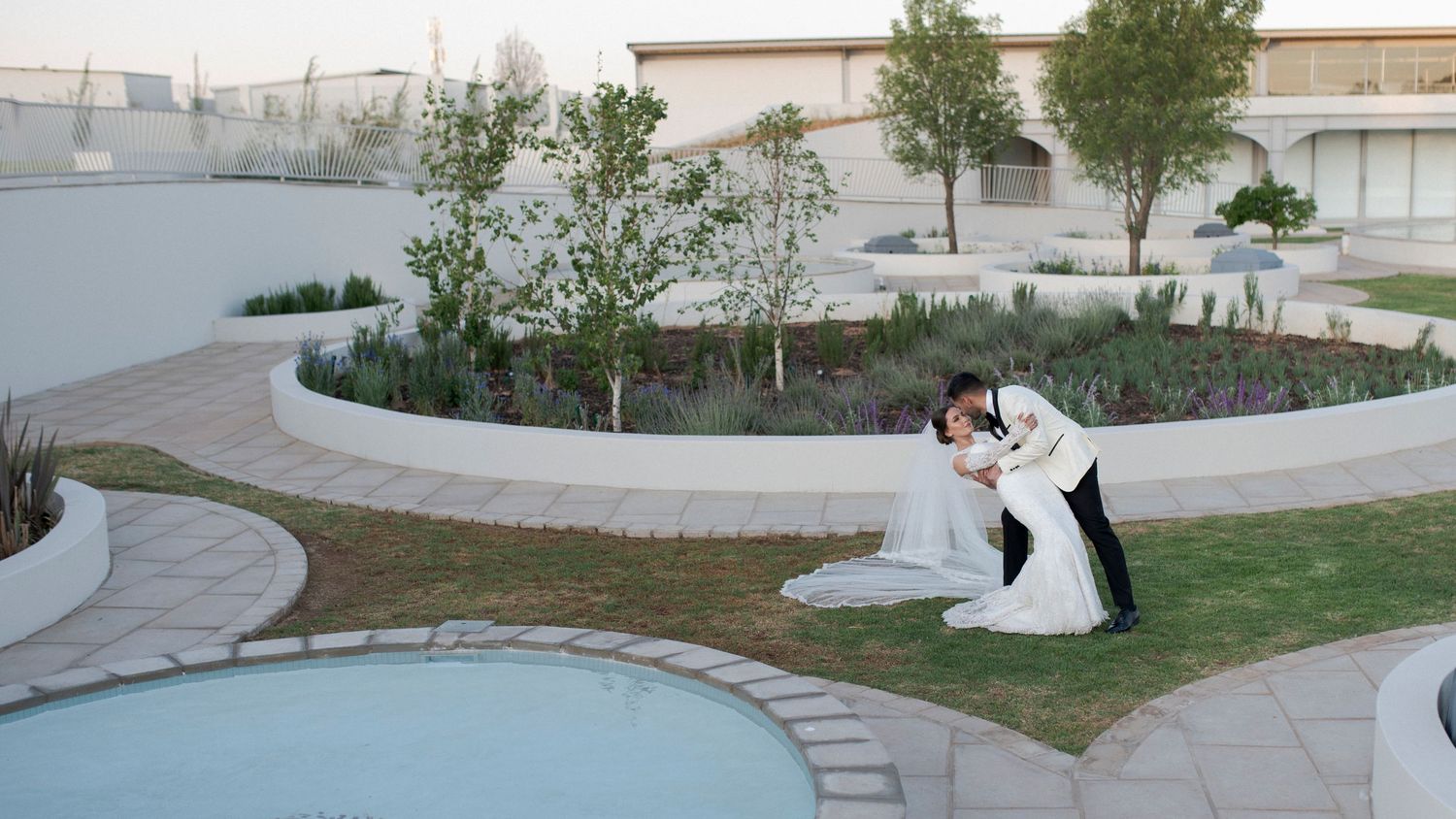 Aerial view of wedding couple dancing on landscaped grounds with curved pathways.