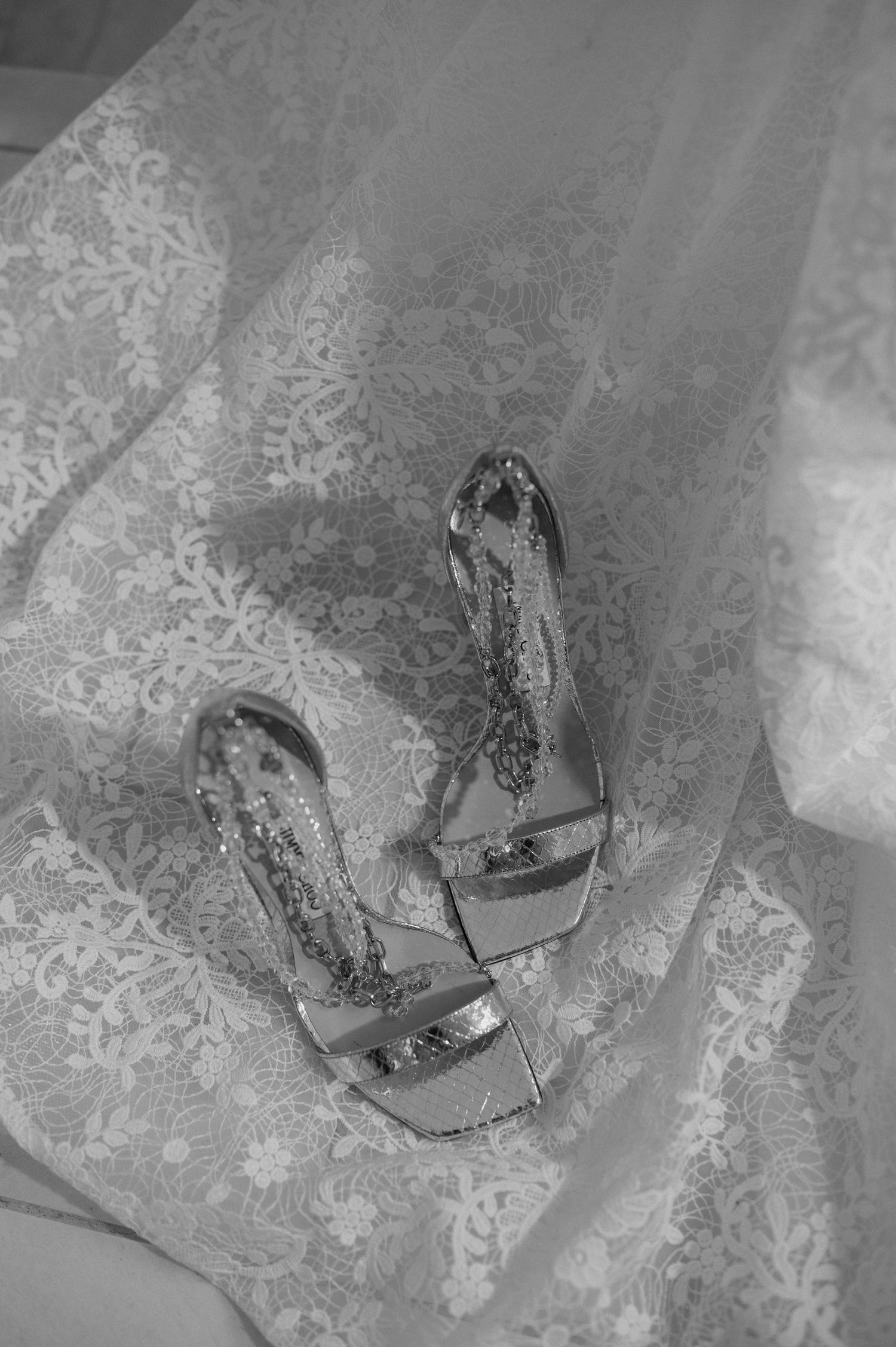 A black and white detail shot of ornate bridal shoes placed on delicate lace fabric.