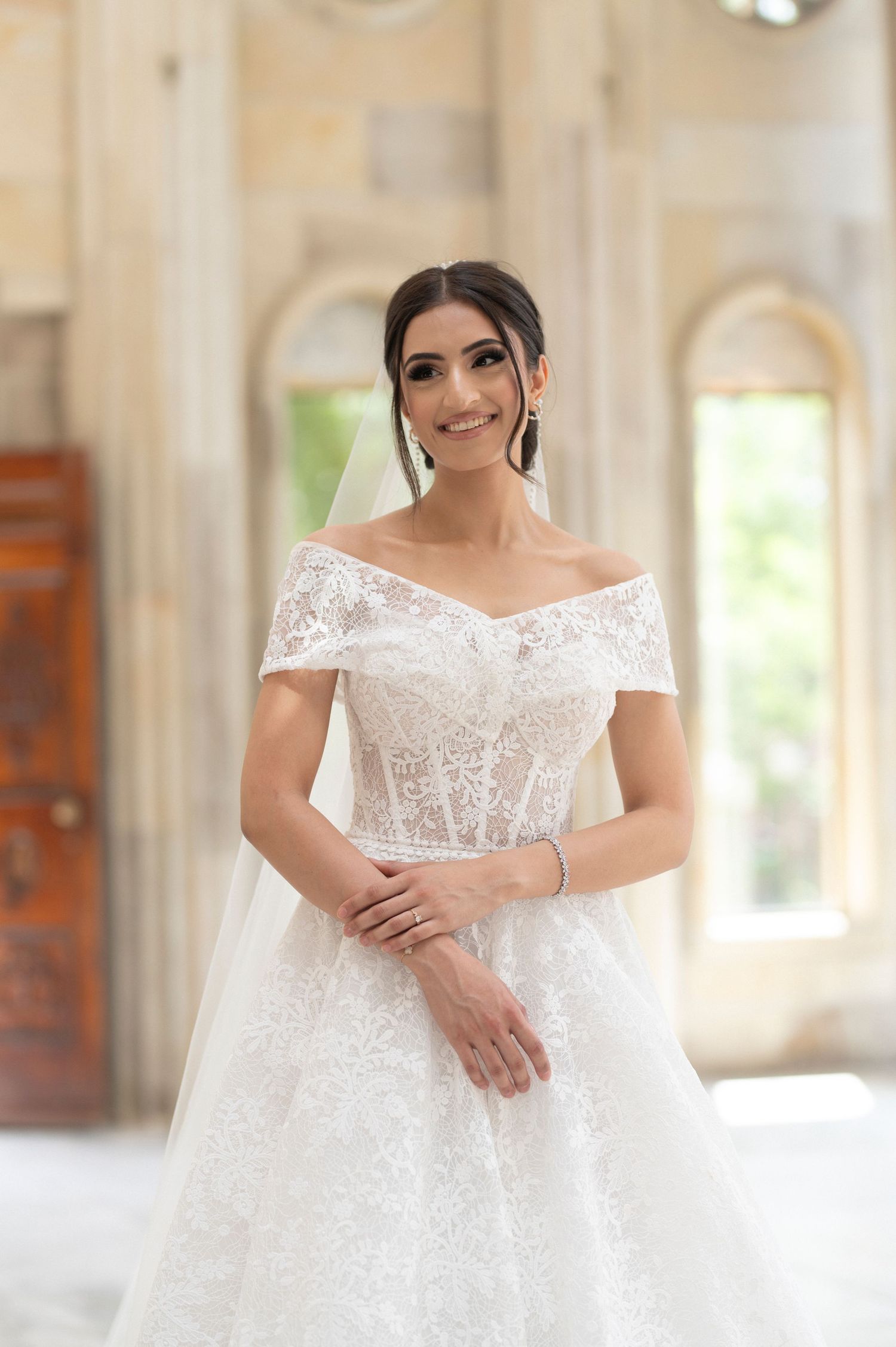 A stunning off-shoulder white lace wedding dress with a corseted bodice photographed in an elegant interior setting.
