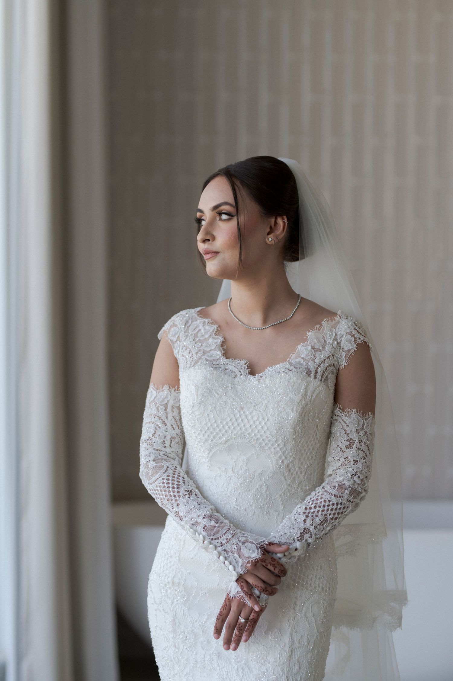 Elegant bridal portrait showcasing lace wedding gown by window light.