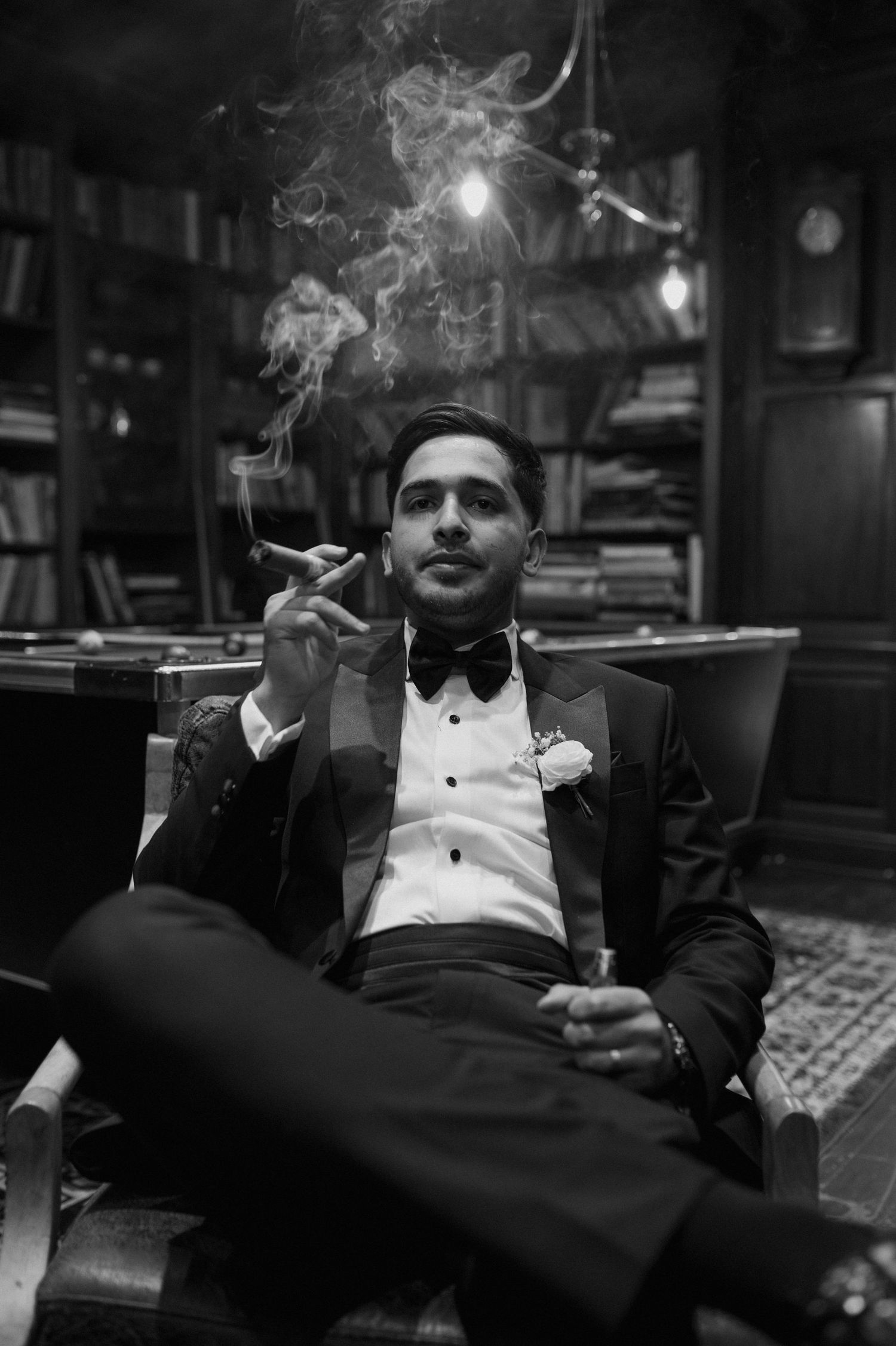 Black and white portrait of someone in formal attire smoking in a dark study.