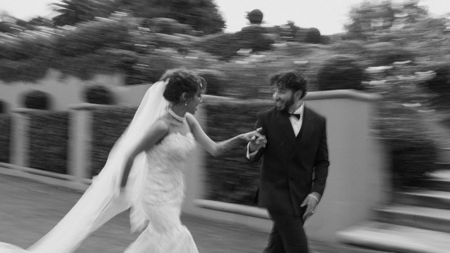 Motion-filled black and white wedding photo with couple dancing on garden path.