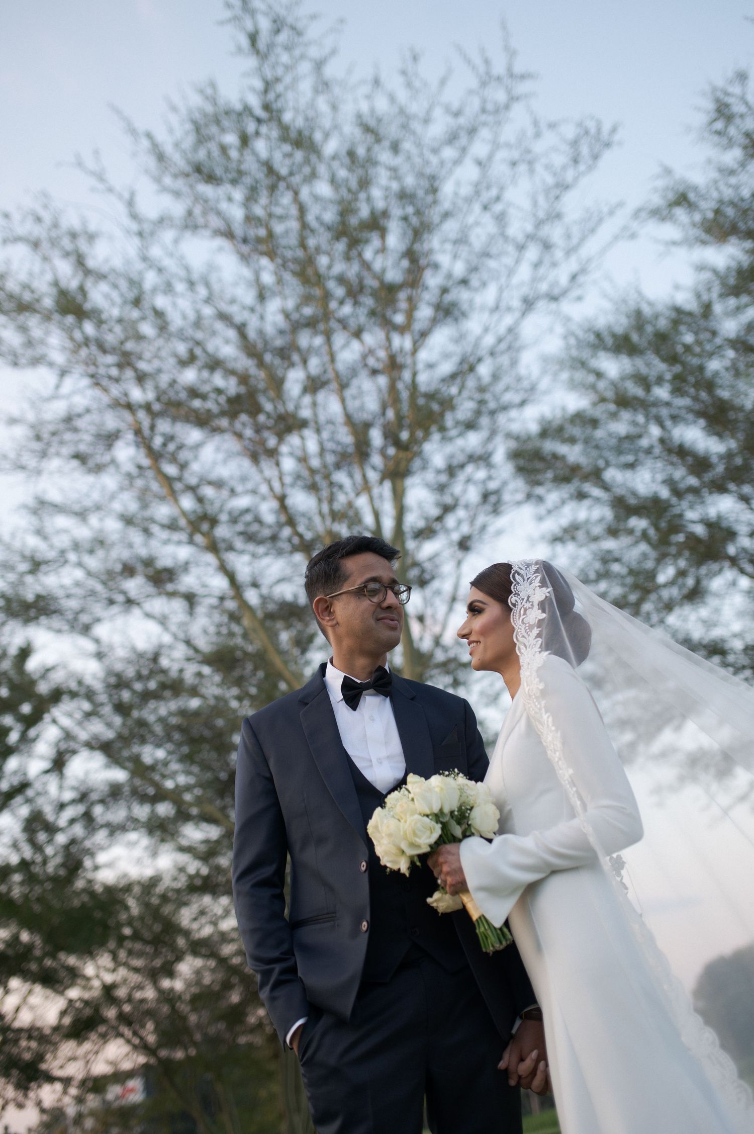 Wedding couple shares intimate moment outdoors with bride holding white bouquet.