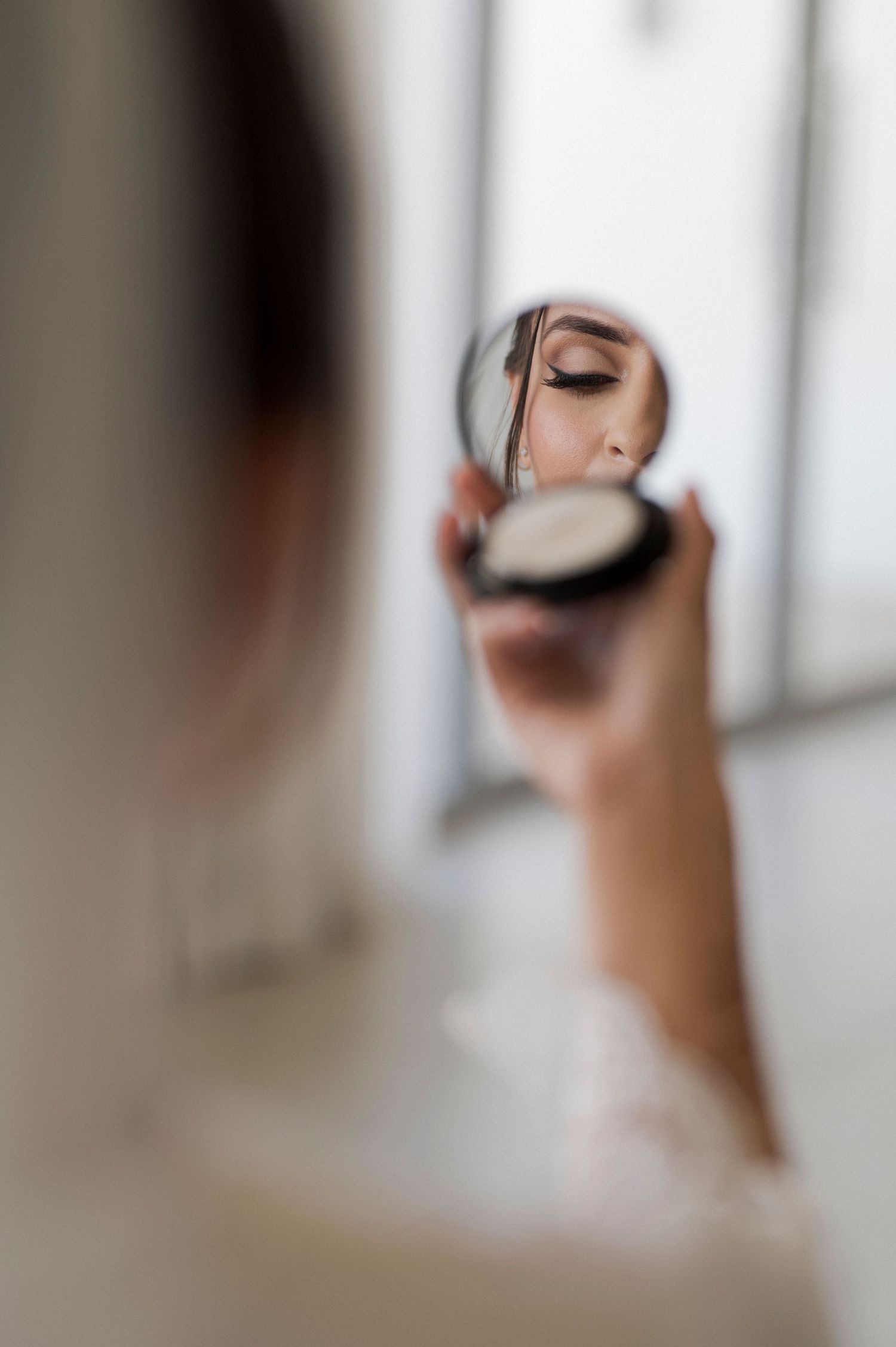 Close-up reflection of bridal makeup application in compact mirror.