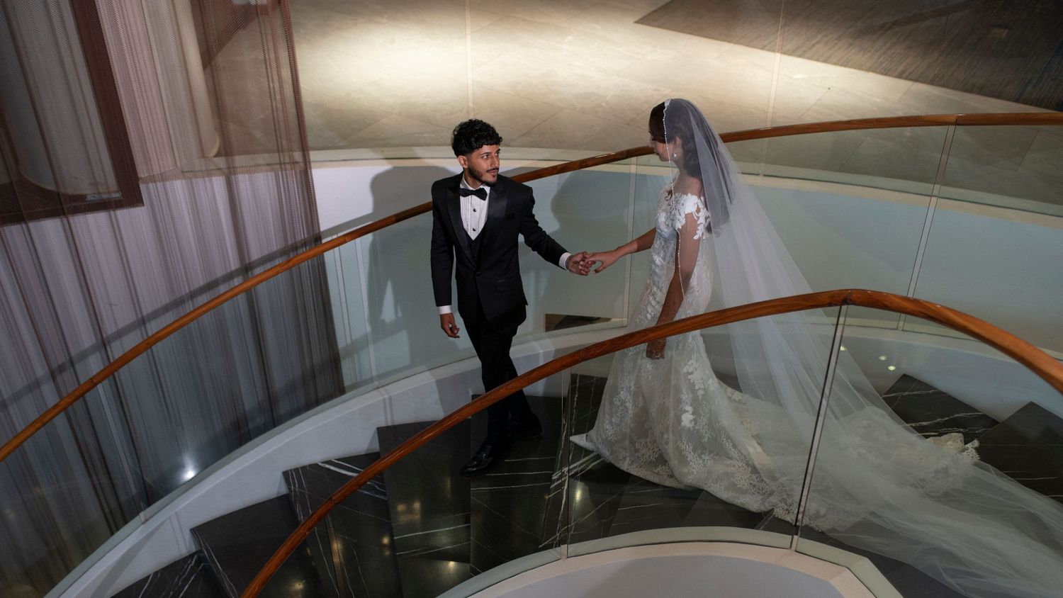 Wedding couple descending a spiral staircase in dramatic lighting.