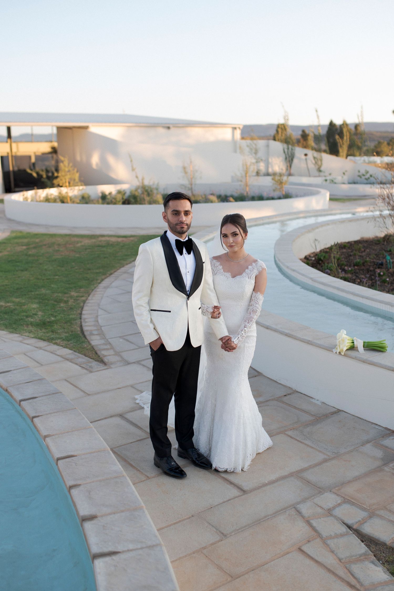 Elegant wedding portrait on curved stone pathway with white architecture.