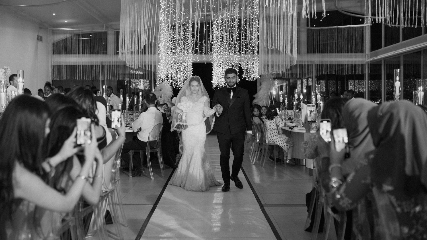 Black and white photograph of a celebration in a modern venue with hanging light curtains.