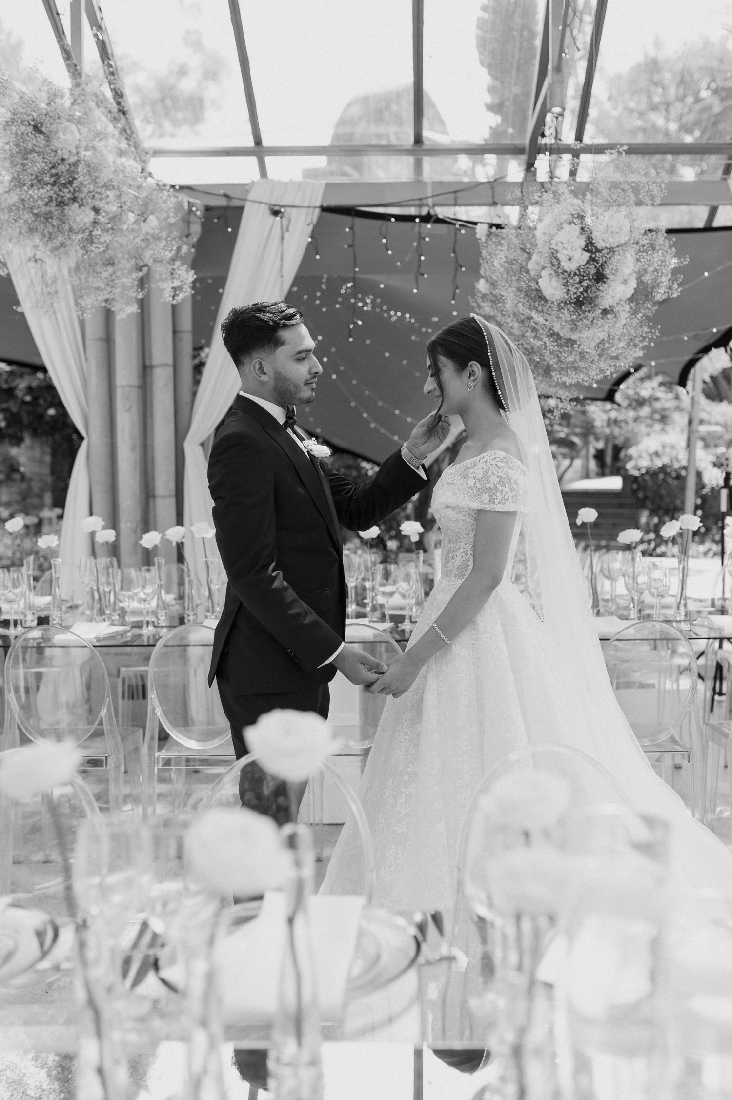 A black and white intimate moment captured between newlyweds at their glass-enclosed reception venue.