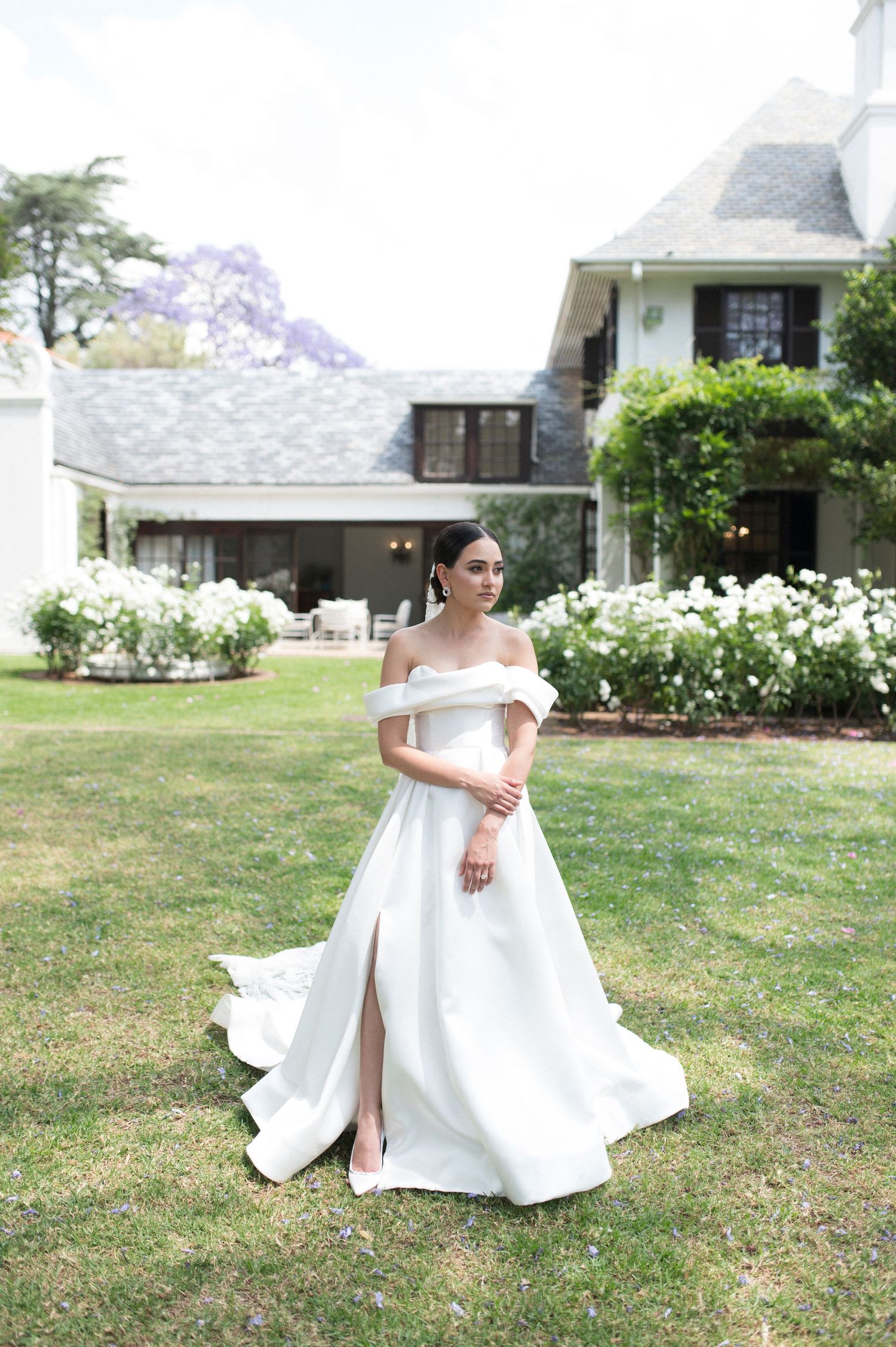 A flowing white off-shoulder wedding gown photographed on a manicured lawn.