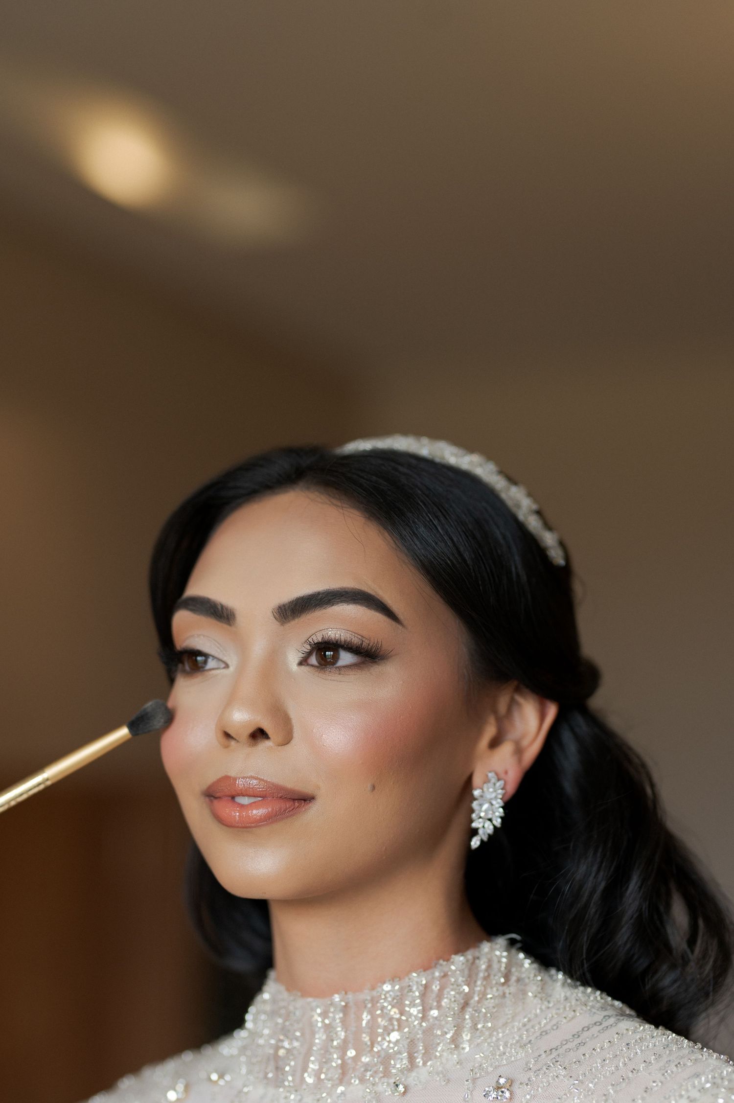 Close-up beauty shot of bride getting final makeup touches while wearing crystal headpiece.