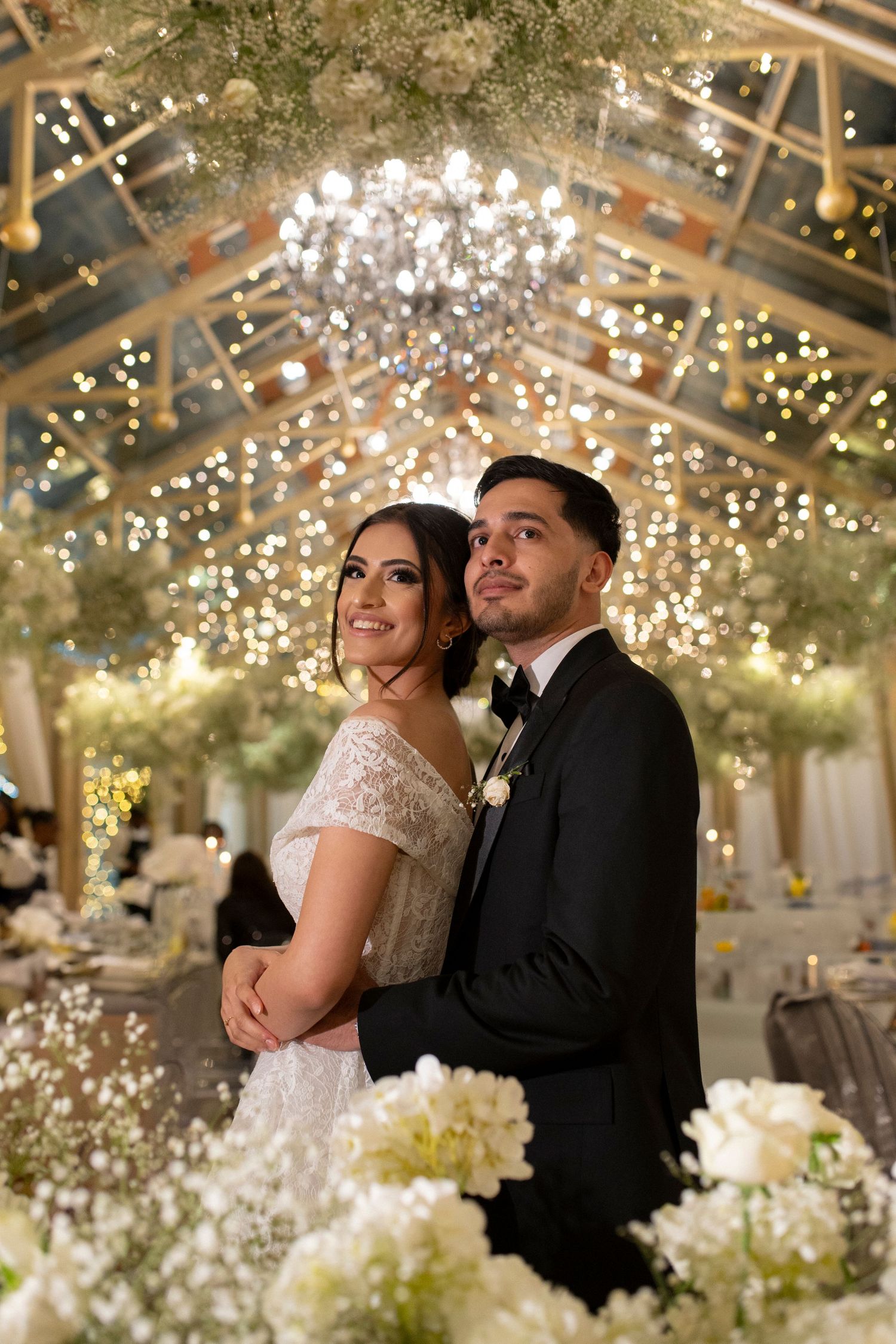 Newlyweds share an intimate moment under twinkling lights and floral ceiling decorations.
