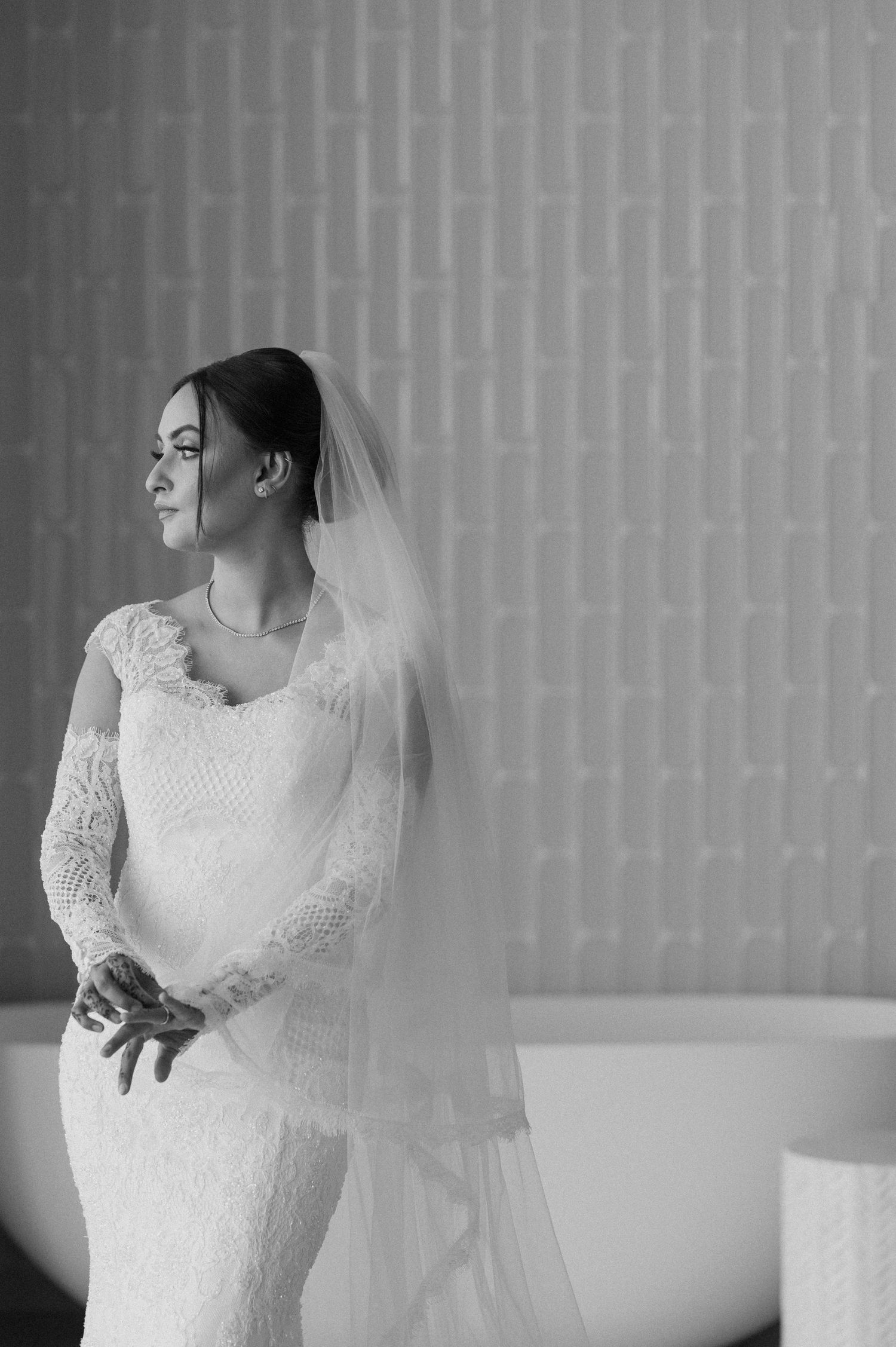 A classic black and white bridal portrait featuring a lace wedding dress and flowing veil against a light background.