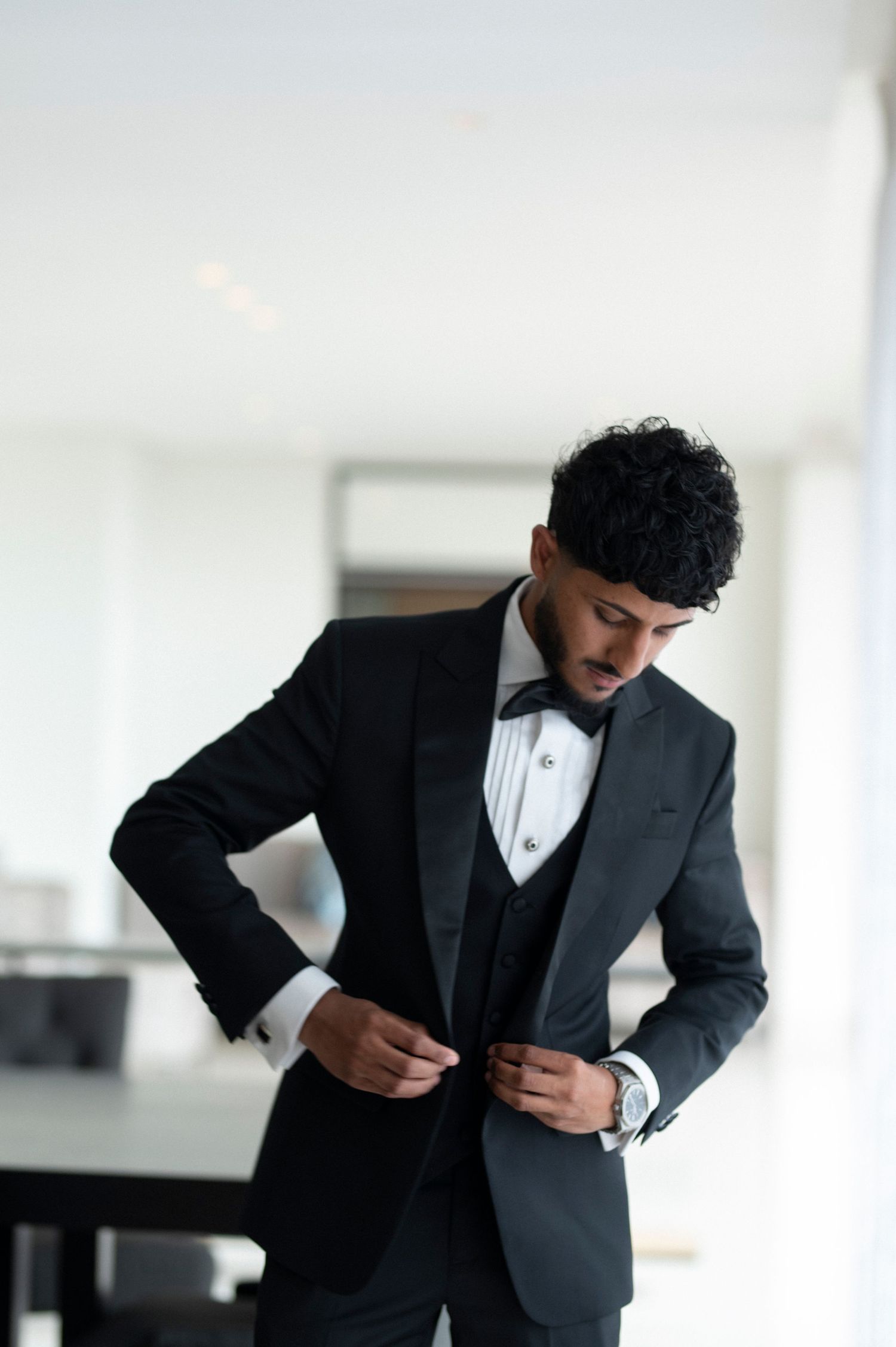 Groom in three-piece tuxedo buttoning his jacket.