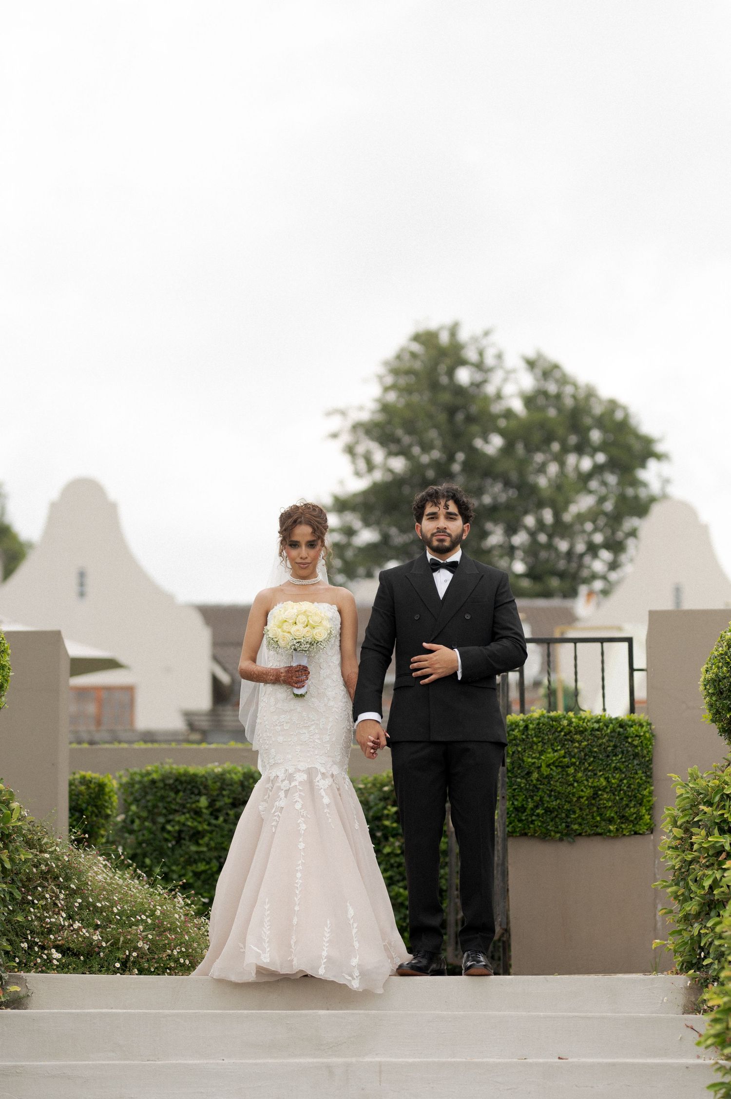Wedding couple poses on outdoor steps with white architectural details.