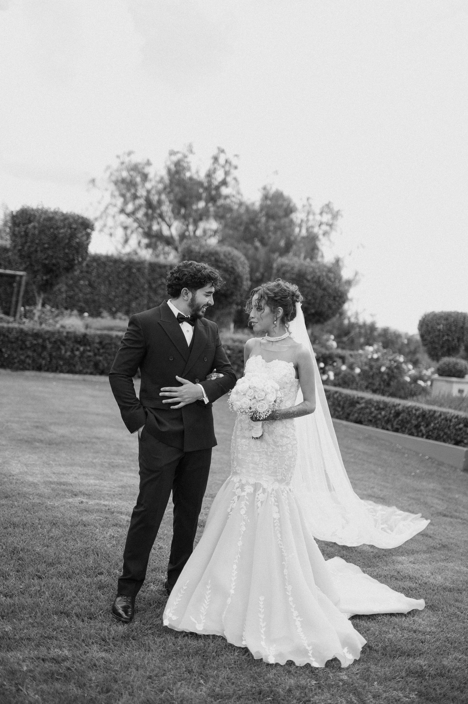 Black and white portrait of newlyweds standing together on a manicured lawn.