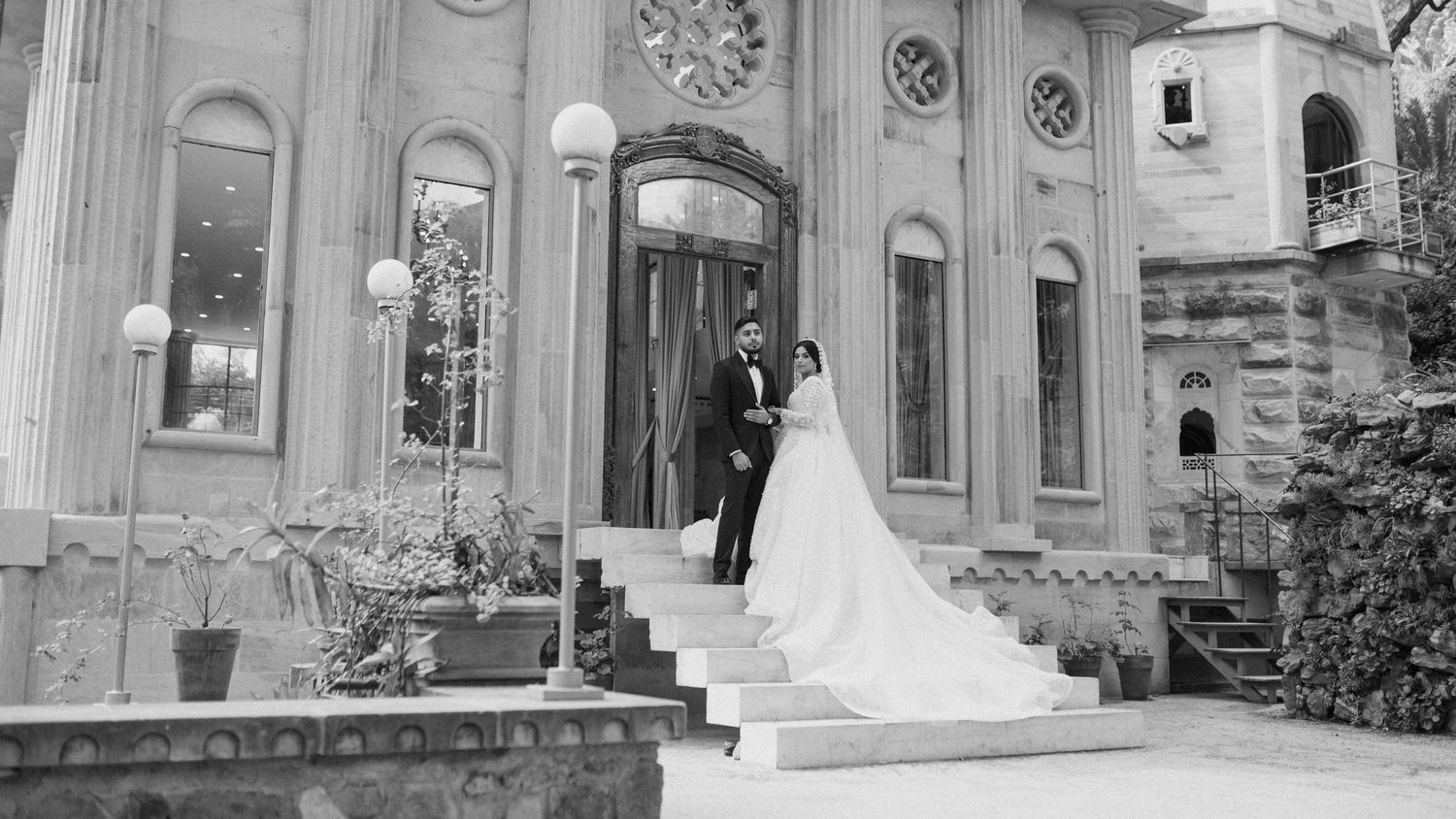 Black and white photo of wedding couple on grand building steps with classical architecture.