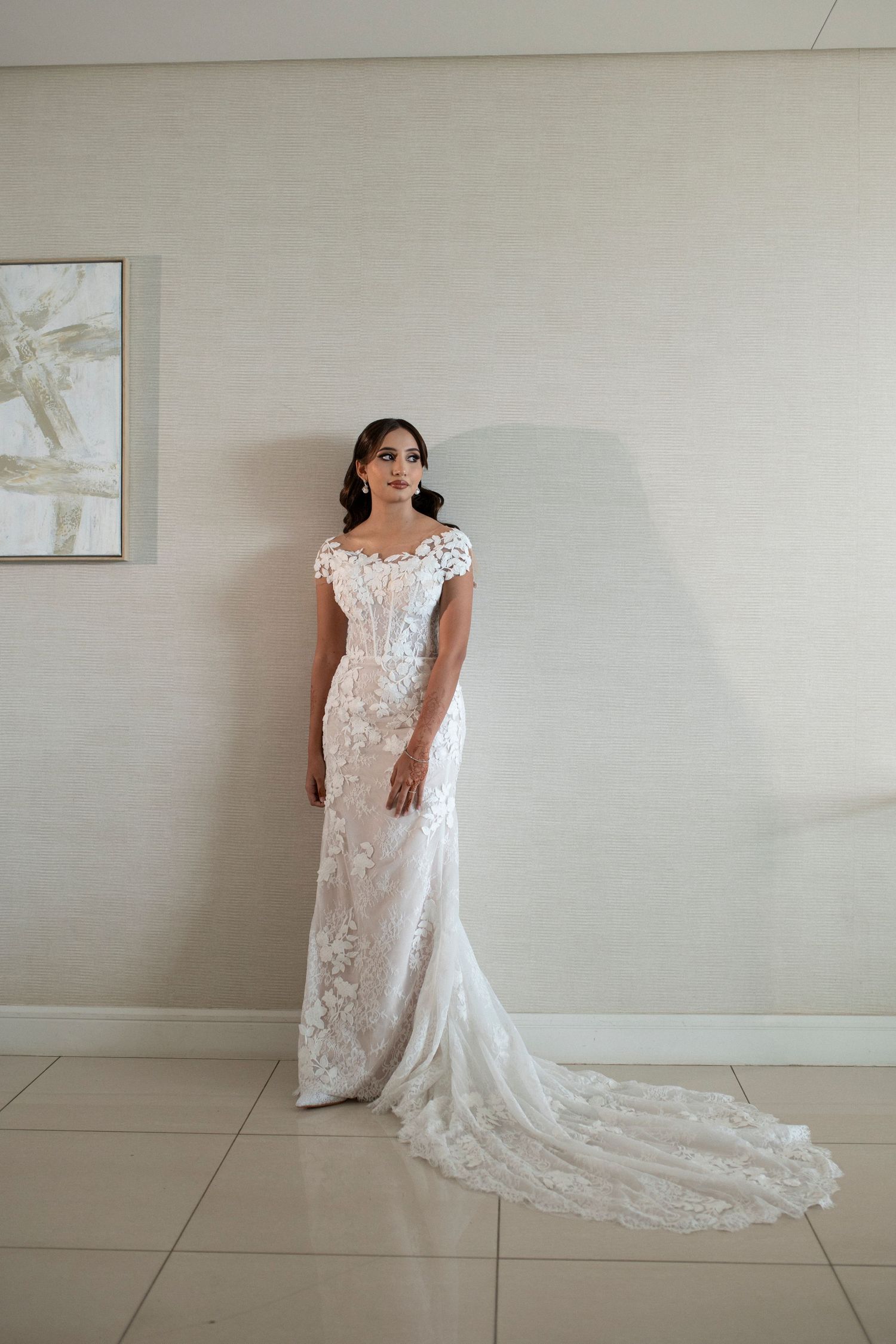 A stunning lace wedding gown with a sweeping train photographed against a light wall.