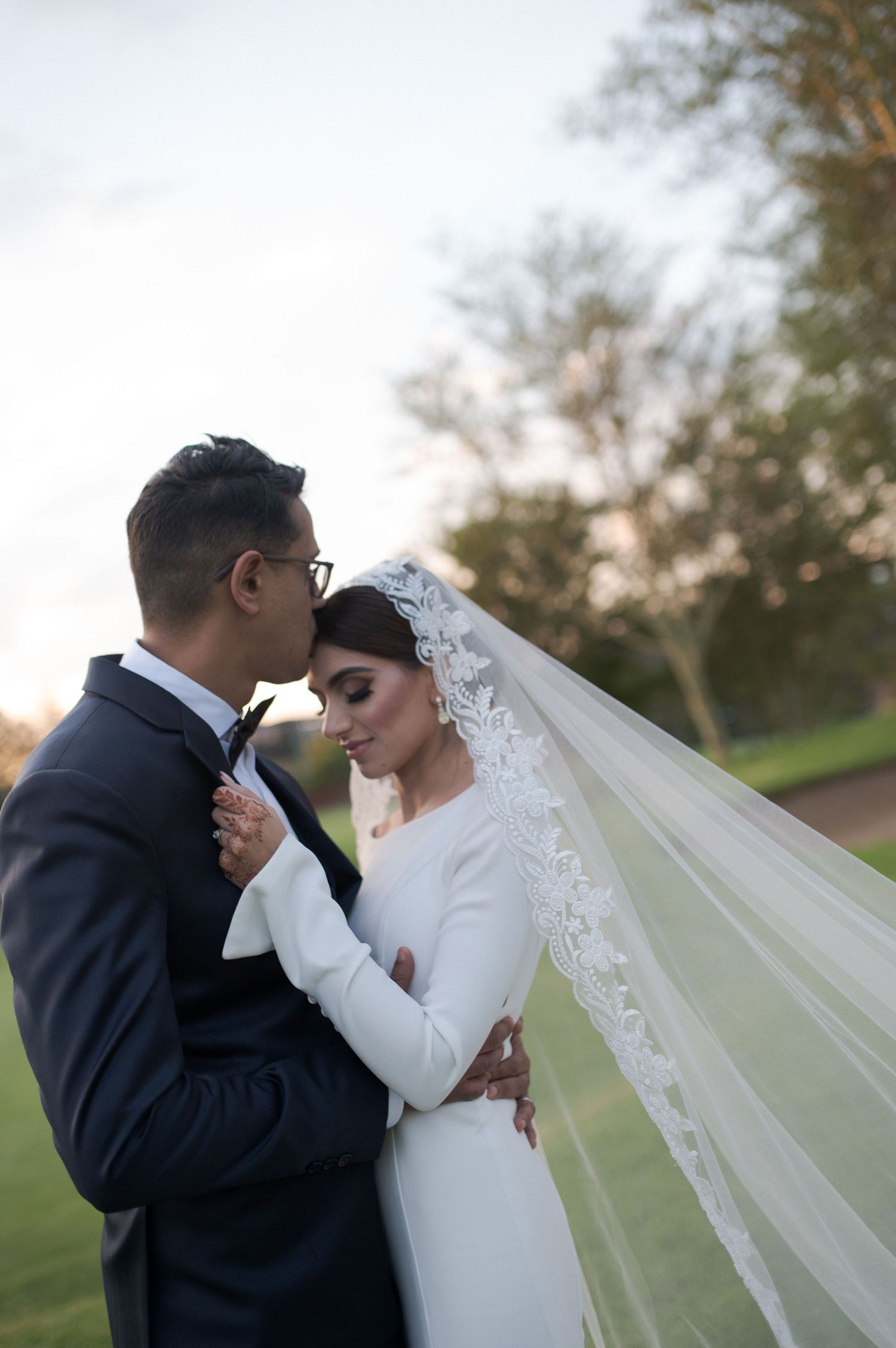 Intimate moment between newlyweds as they embrace outdoors with bride's veil flowing in the breeze.