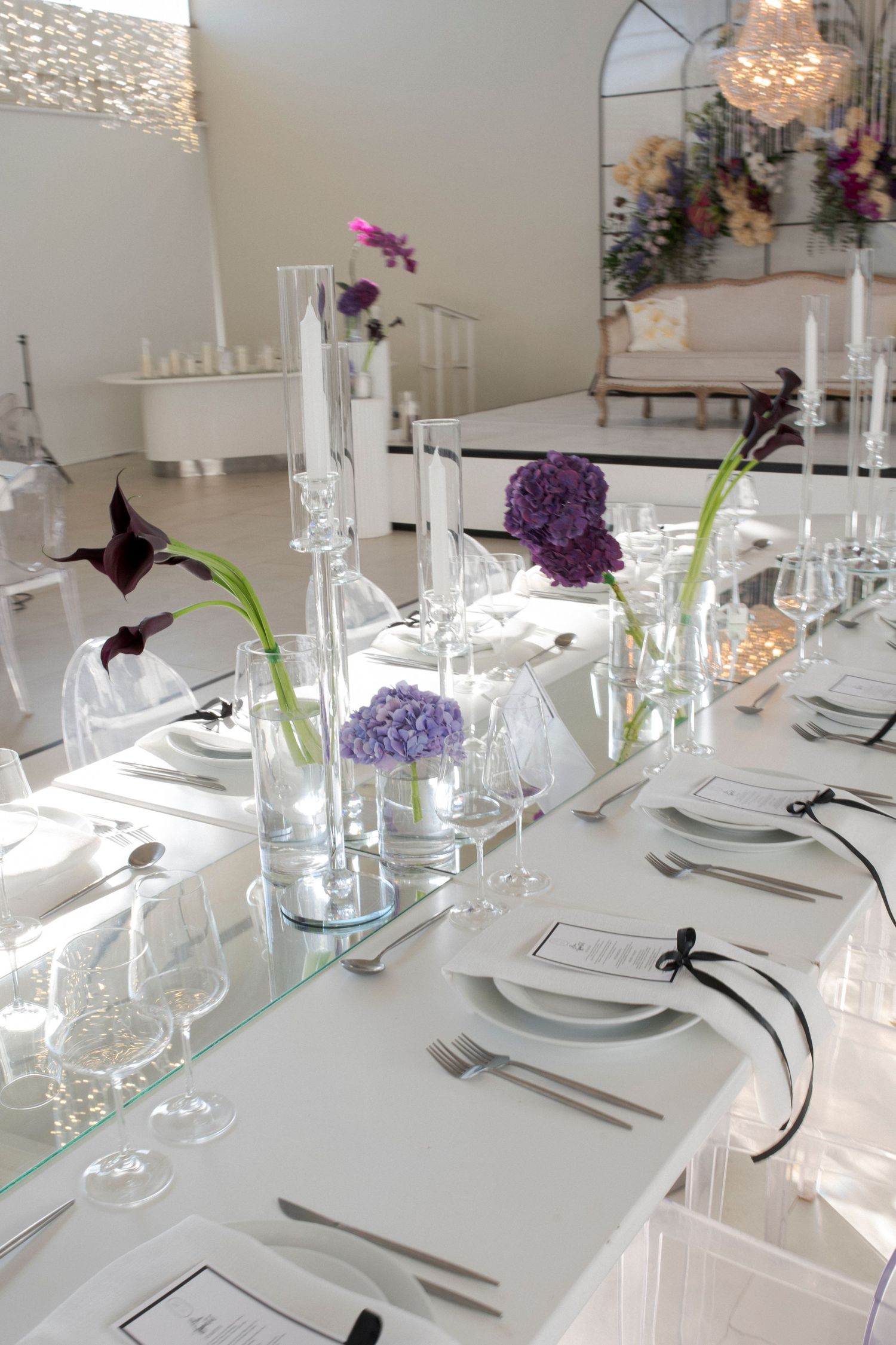 Modern wedding table setup with purple flowers and white place settings in bright venue.