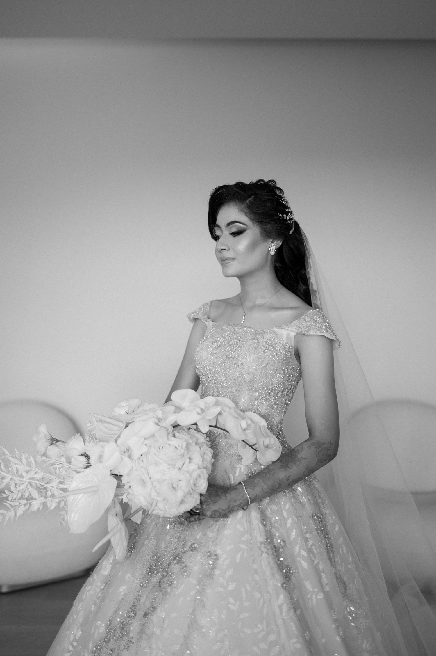 Black and white portrait of bride with floral bouquet in luxurious beaded gown.