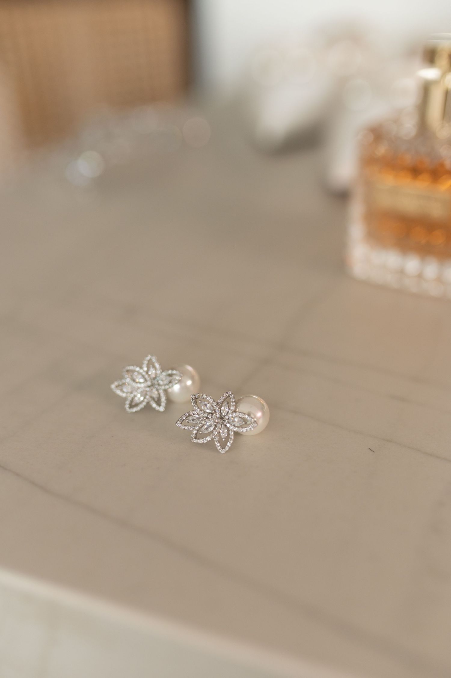 Delicate floral silver earrings displayed next to a luxury perfume bottle.