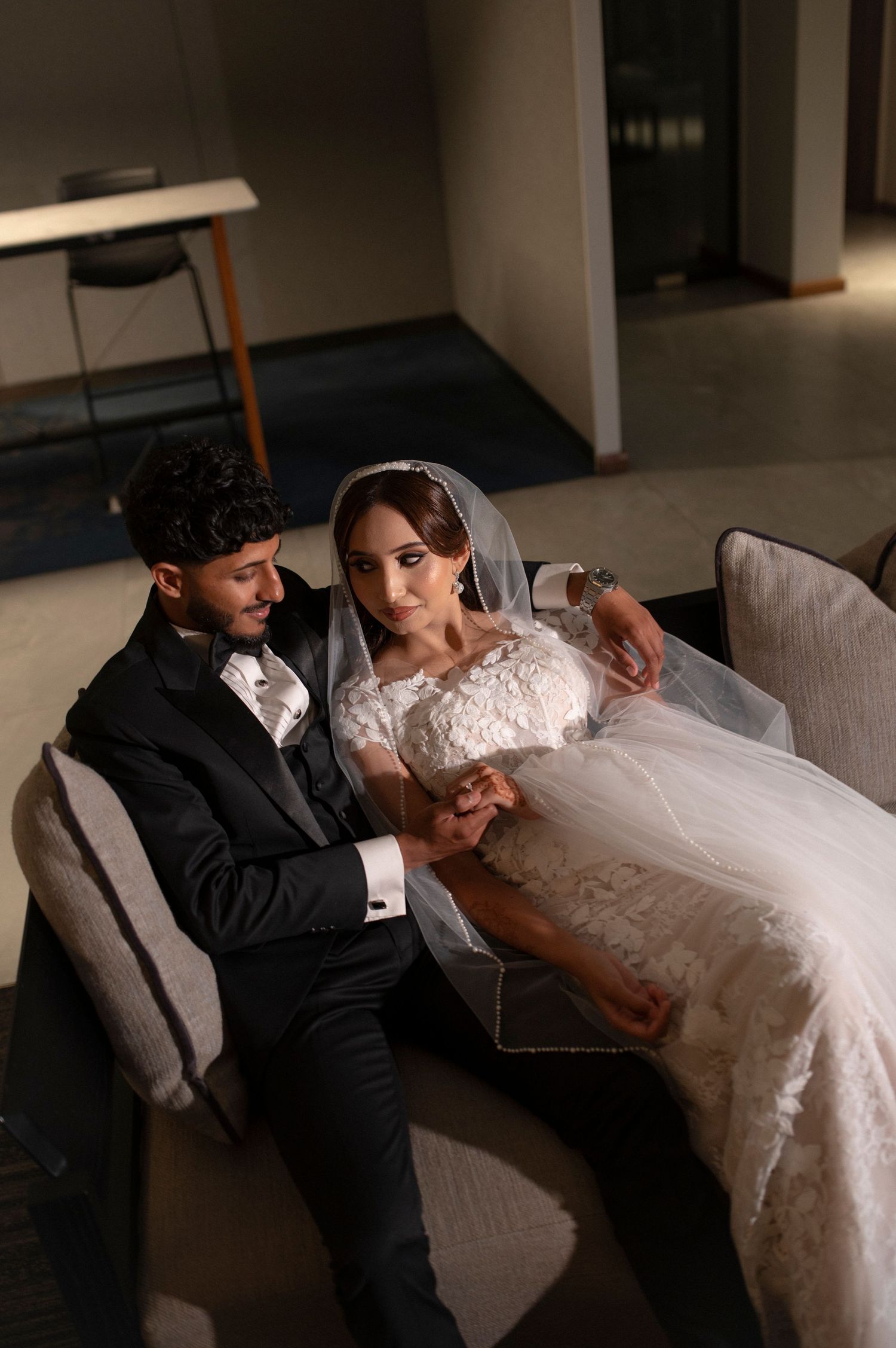 Intimate moment of newlyweds relaxing on a gray couch in formal attire.