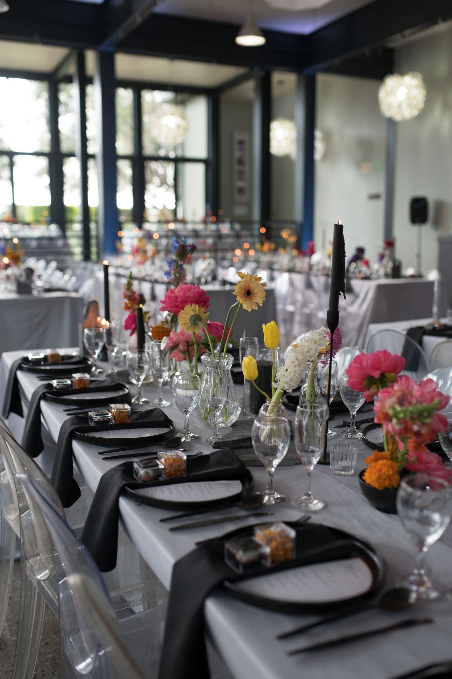 Modern wedding table setting with colorful floral centerpieces and black place settings on gray linens.