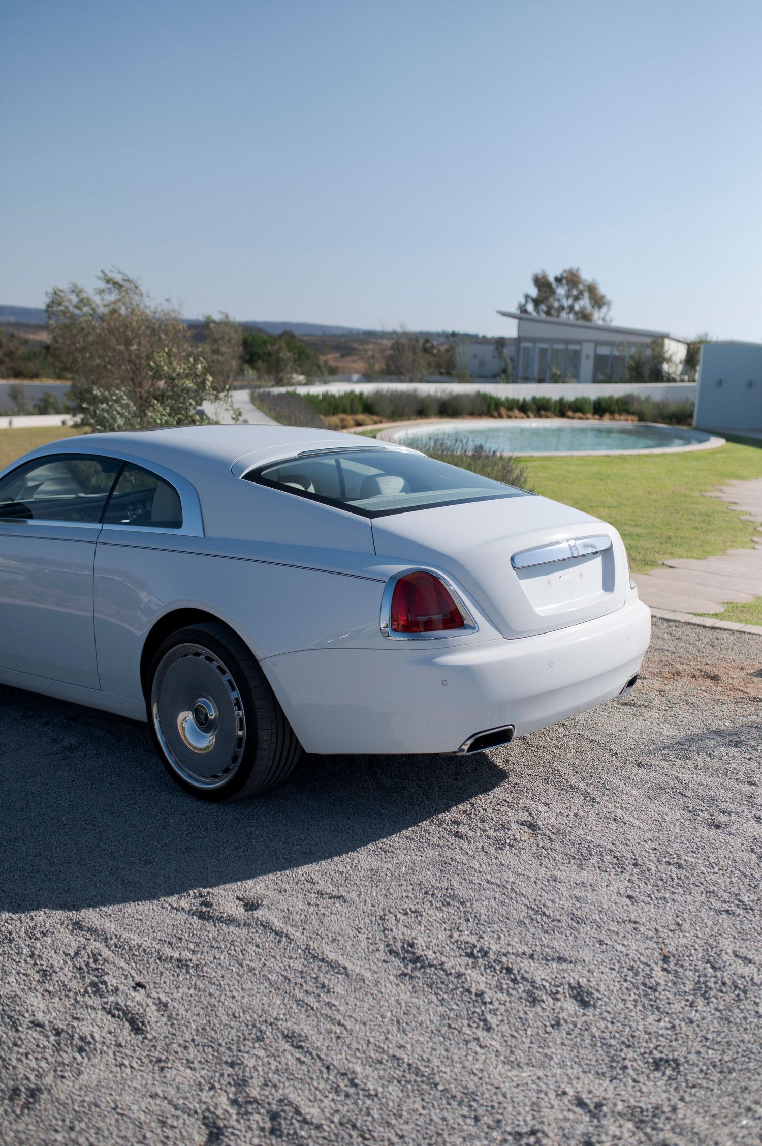 Luxury white Rolls Royce parked outdoors with scenic mountain backdrop.