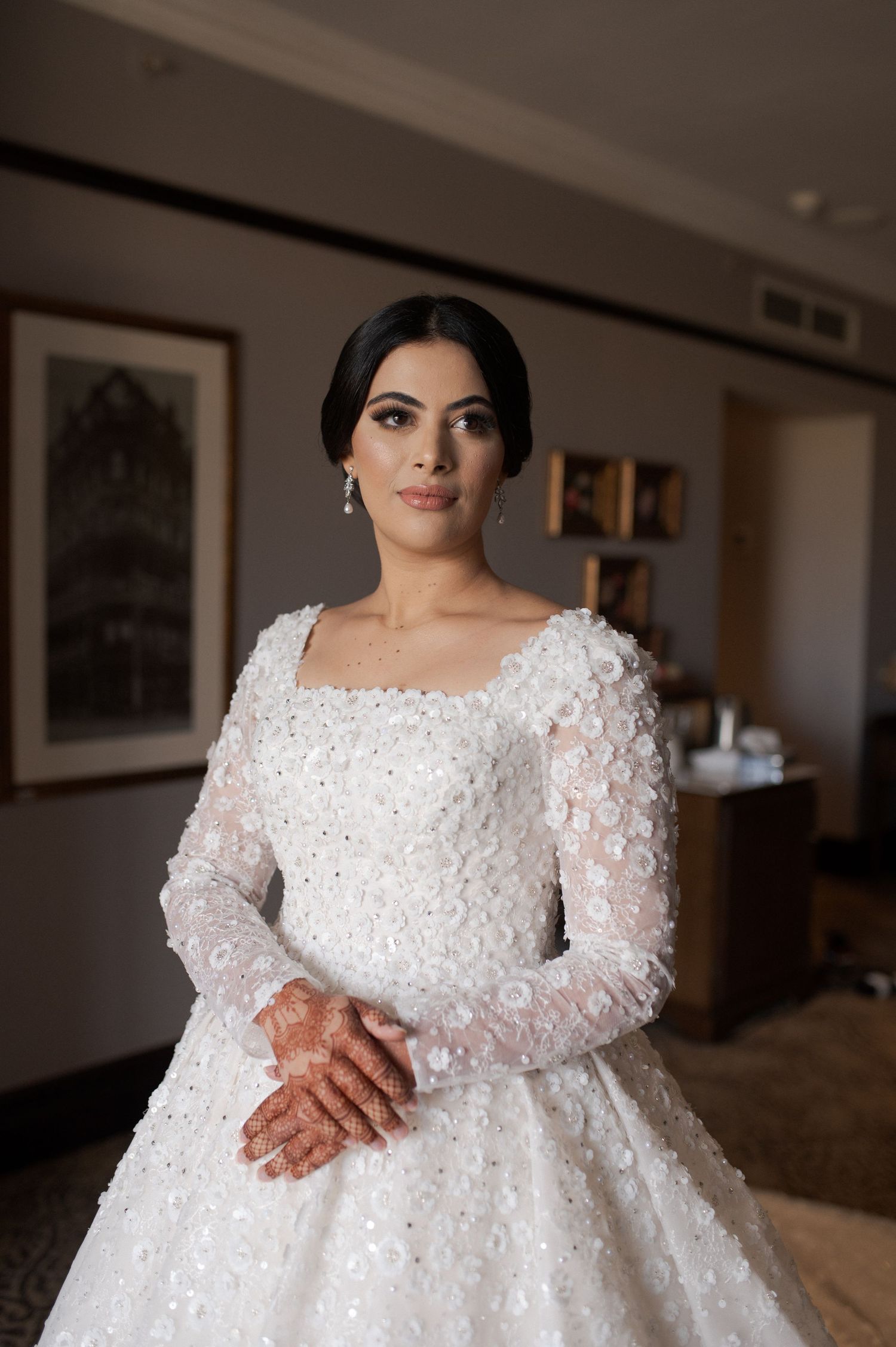 A bride poses in a long-sleeved ball gown featuring intricate floral appliques.