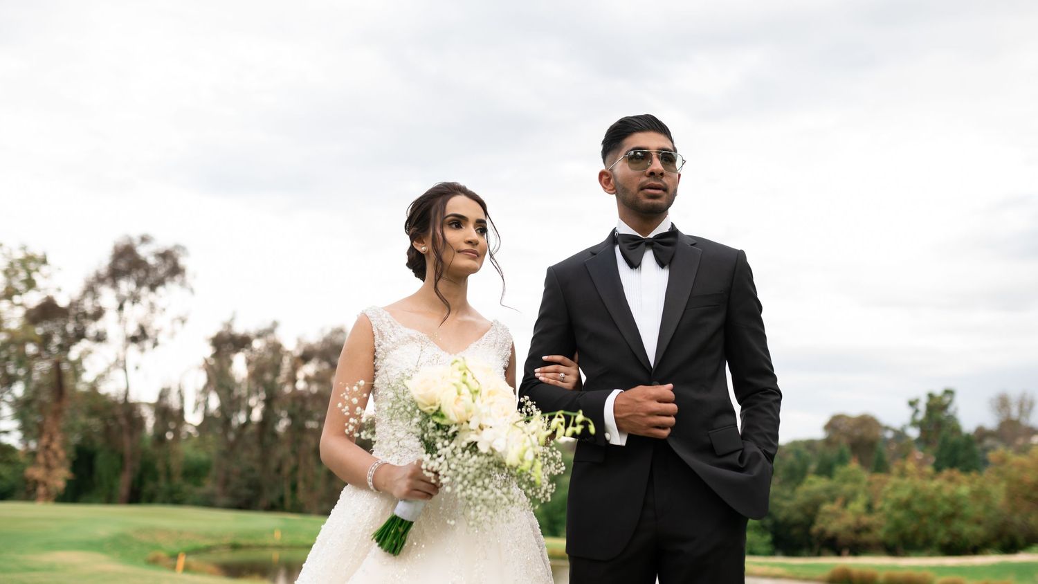 A wedding couple poses together outdoors with natural greenery in the background.