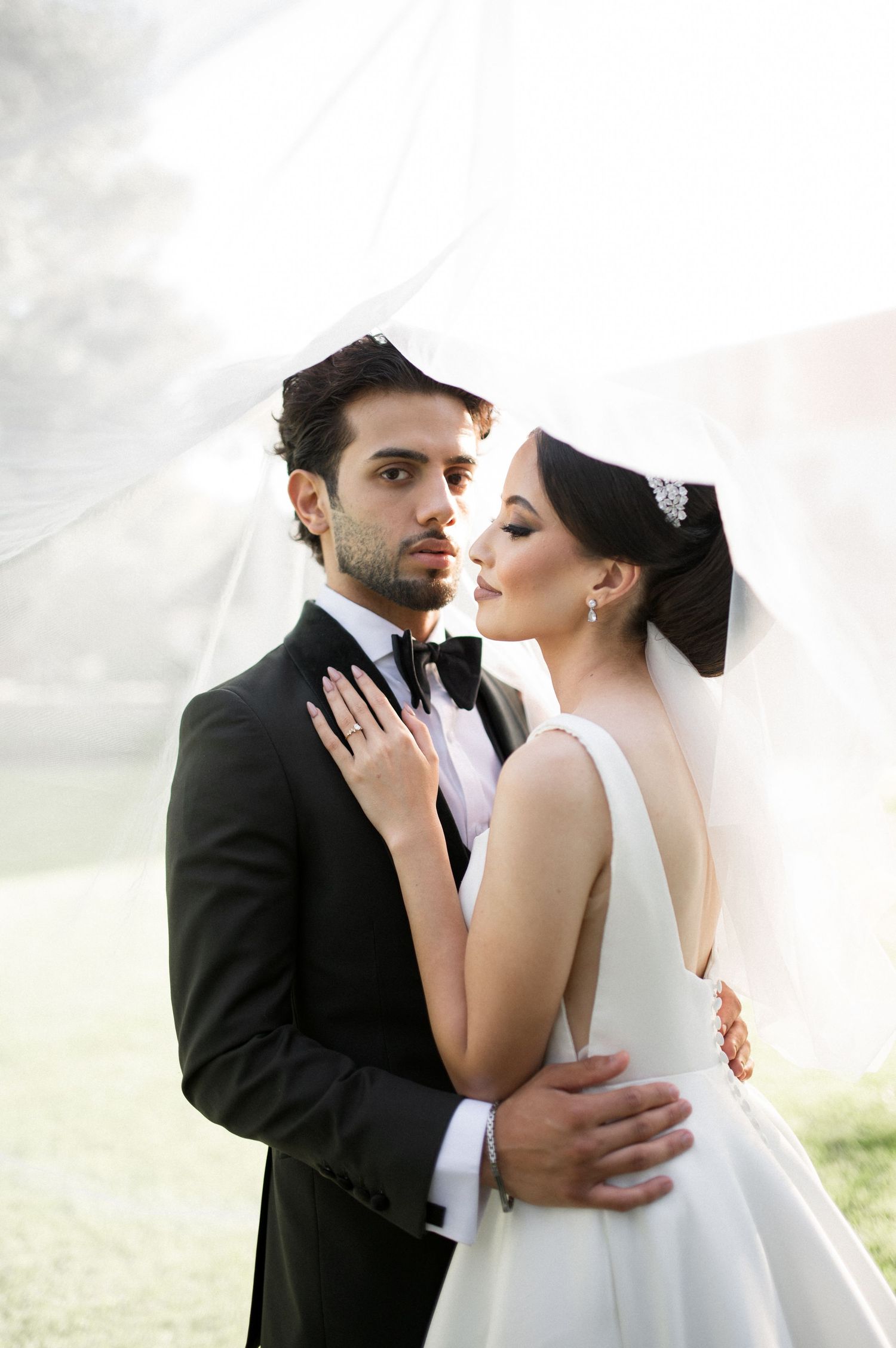 A romantic wedding portrait showing the couple in an intimate embrace against a bright background.