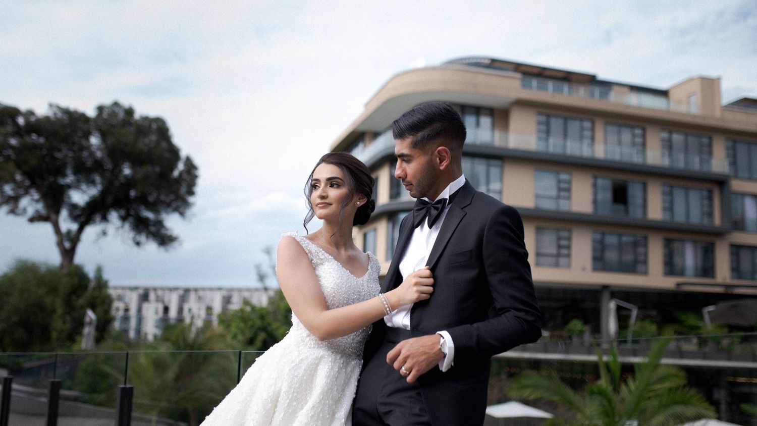 Wedding couple embracing on terrace with modern architecture in background.