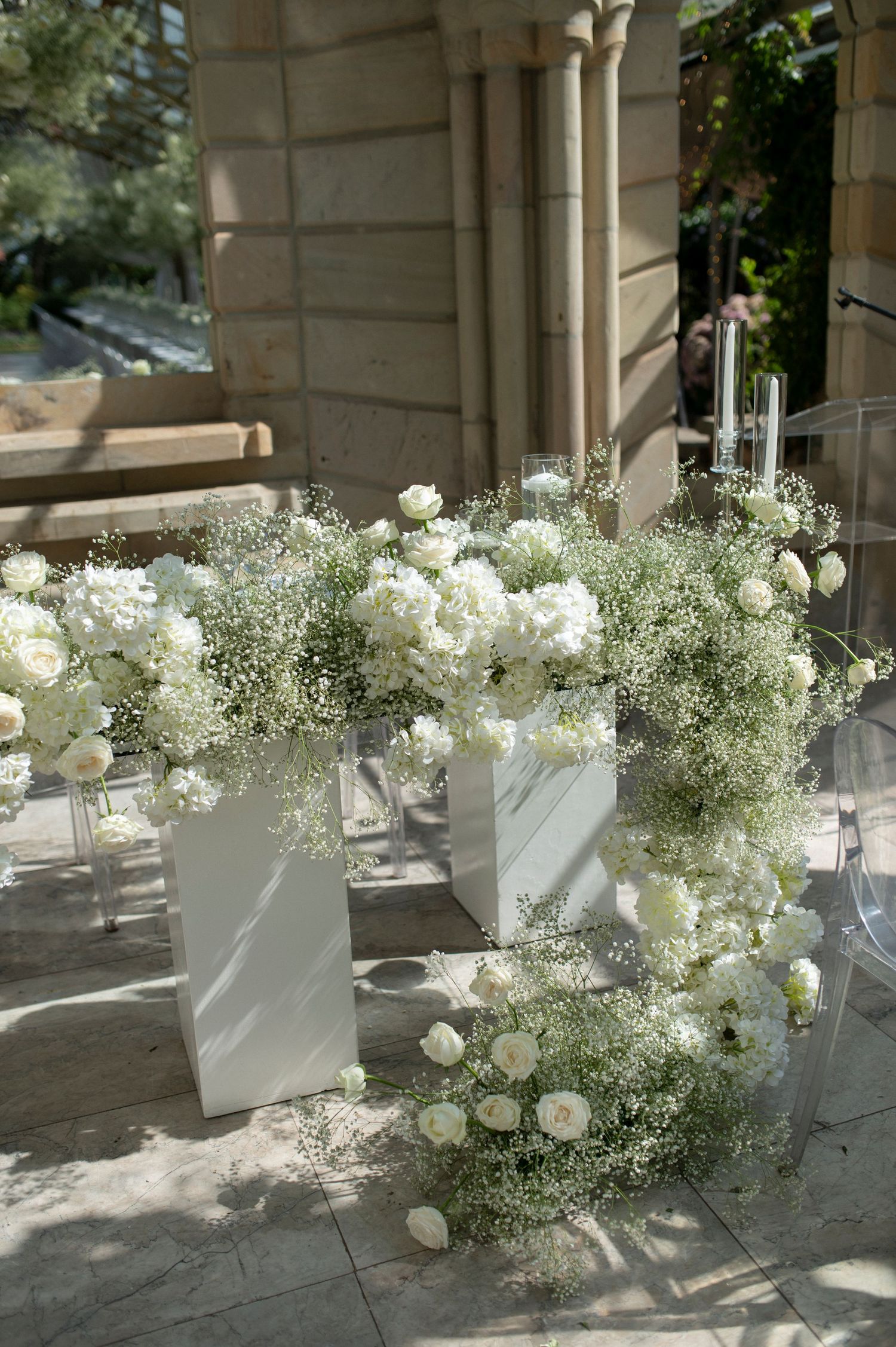 White floral arrangements with delicate baby's breath decorate a stone patio with tall candles.