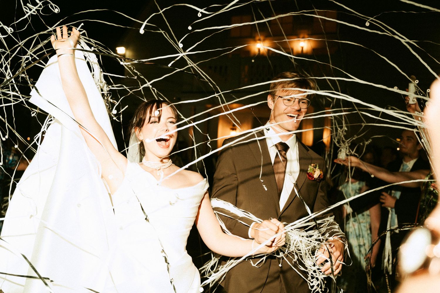 Joyful bride and groom exit wedding reception through cascading streamers, celebrating their special night.