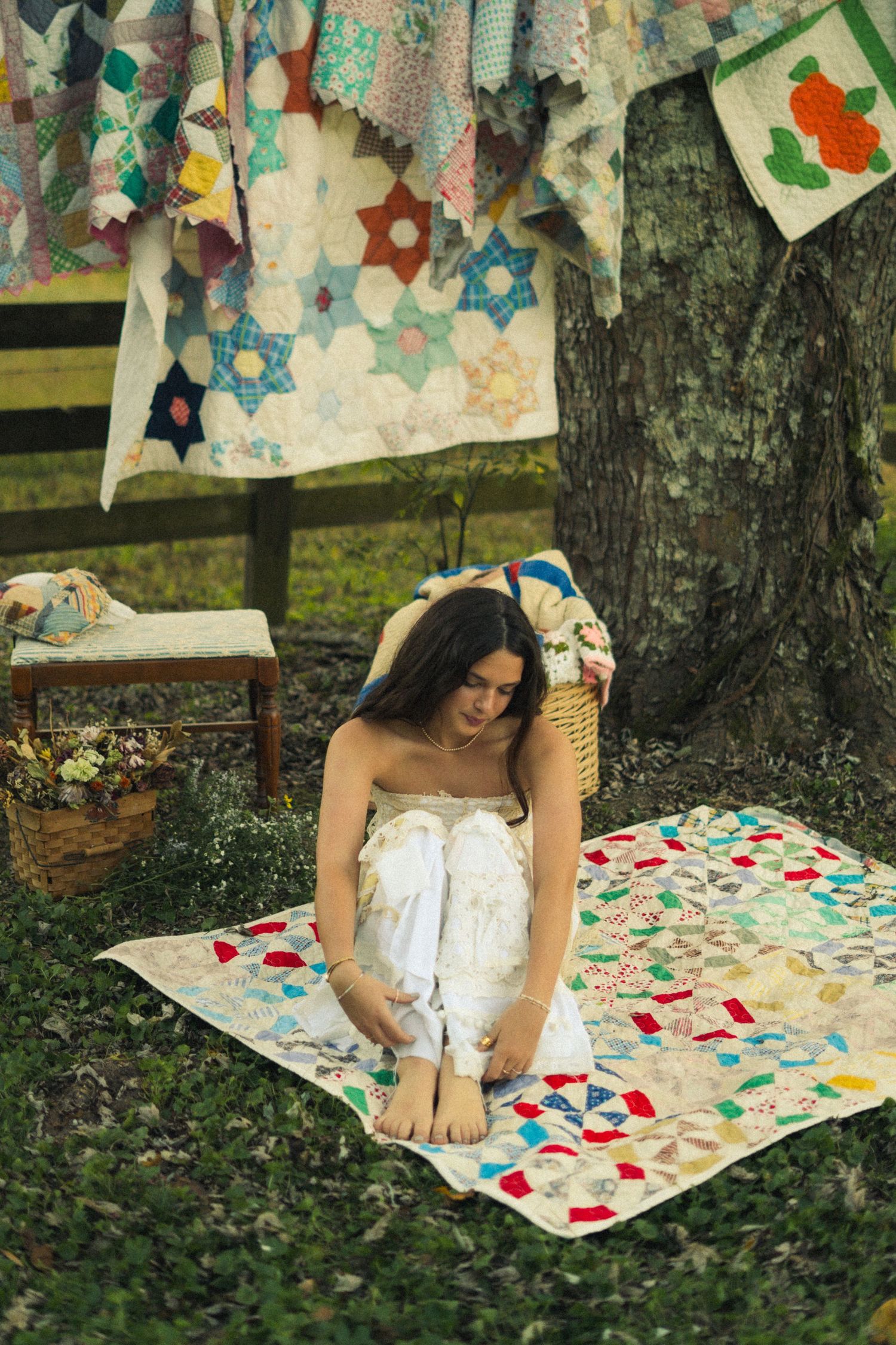Person in white dress sitting on a colorful patterned blanket outdoors with paper decorations hanging above.