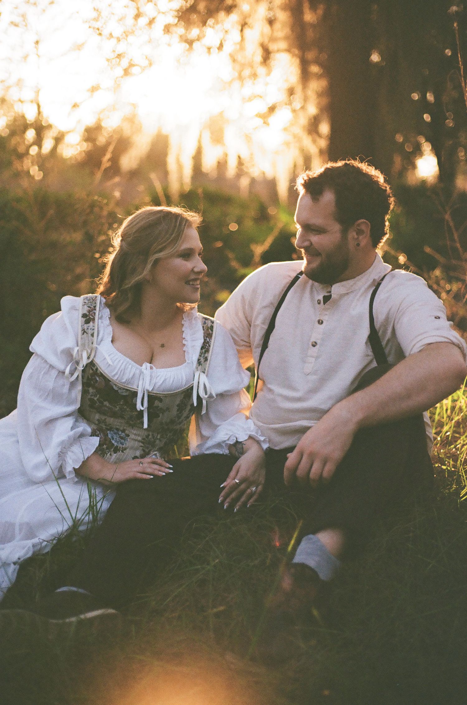 A romantic sunset portrait in a field with golden backlighting through trees.